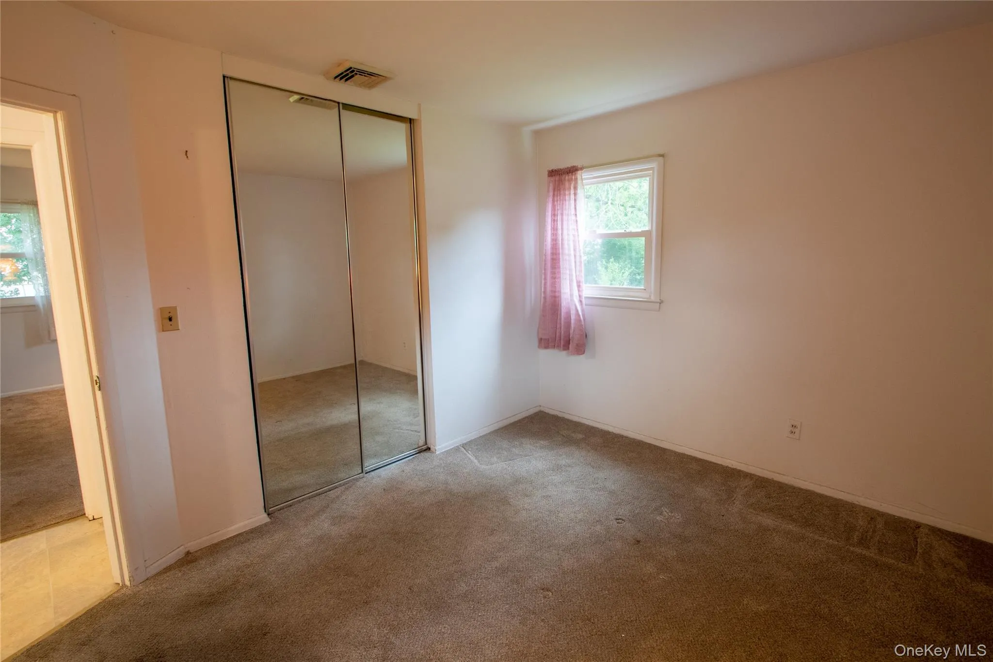 Room with carpet flooring, a window with exterior views, and a mirrored closet Room with carpet flooring, a window with exterior views, and a mirrored closet