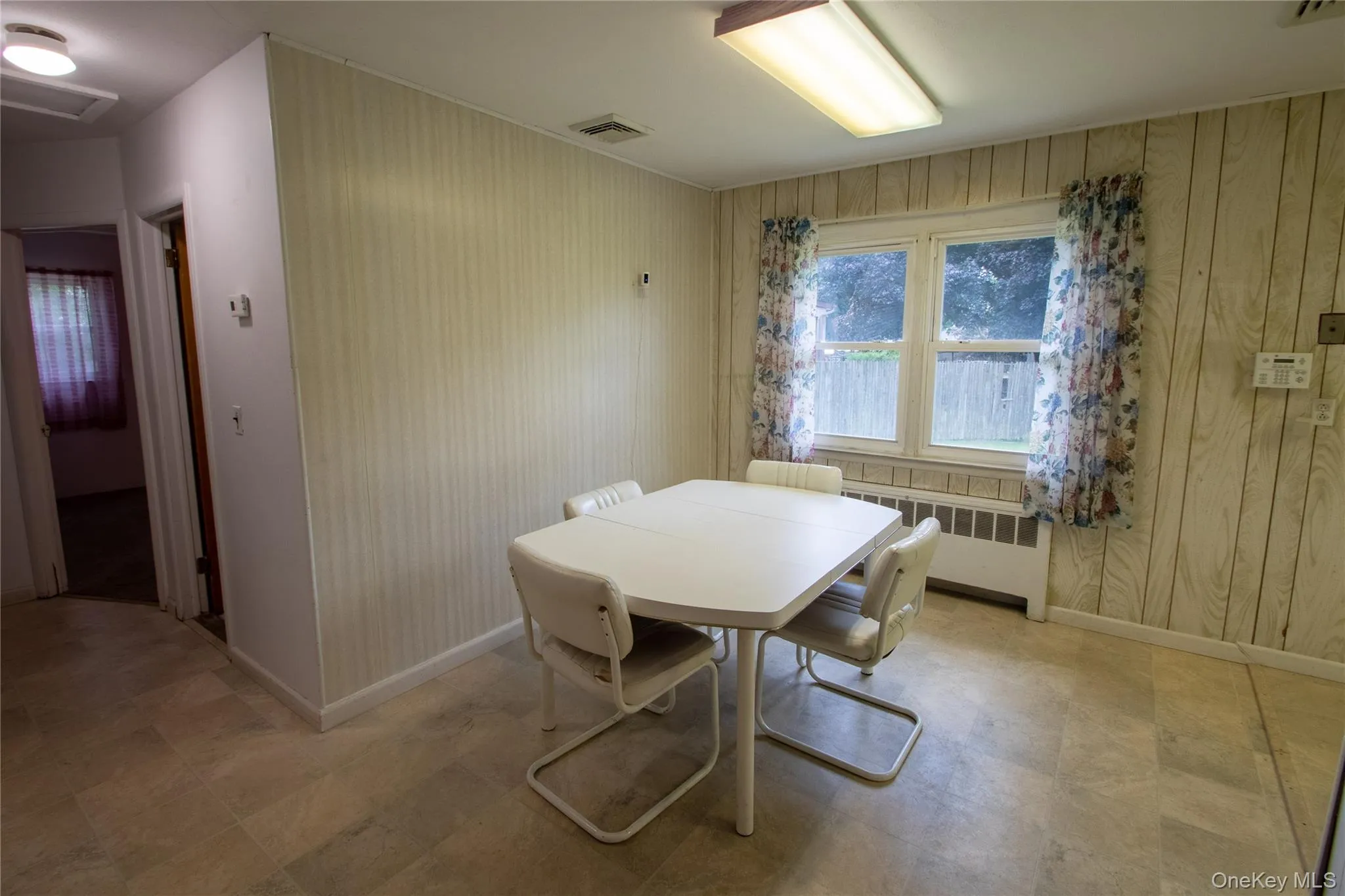Dining area featuring a double window, wood-finish wall paneling, and a flush-mount ceiling light Dining area featuring a double window, wood-finish wall paneling, and a flush-mount ceiling light