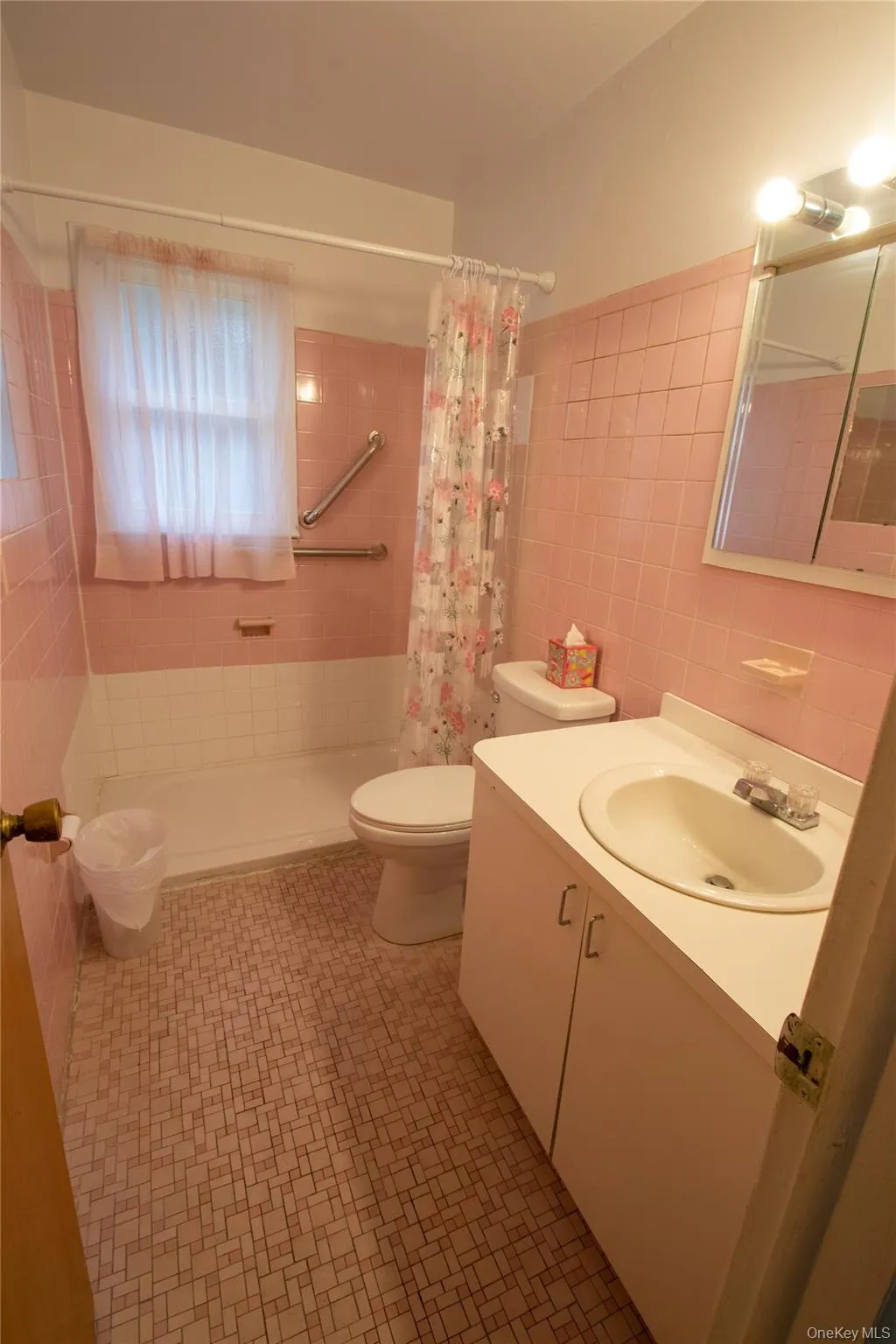 Bathroom featuring pink wall tiling, white bathtub, white toilet, and a white vanity with an integrated sink Bathroom featuring pink wall tiling, white bathtub, white toilet, and a white vanity with an integrated sink