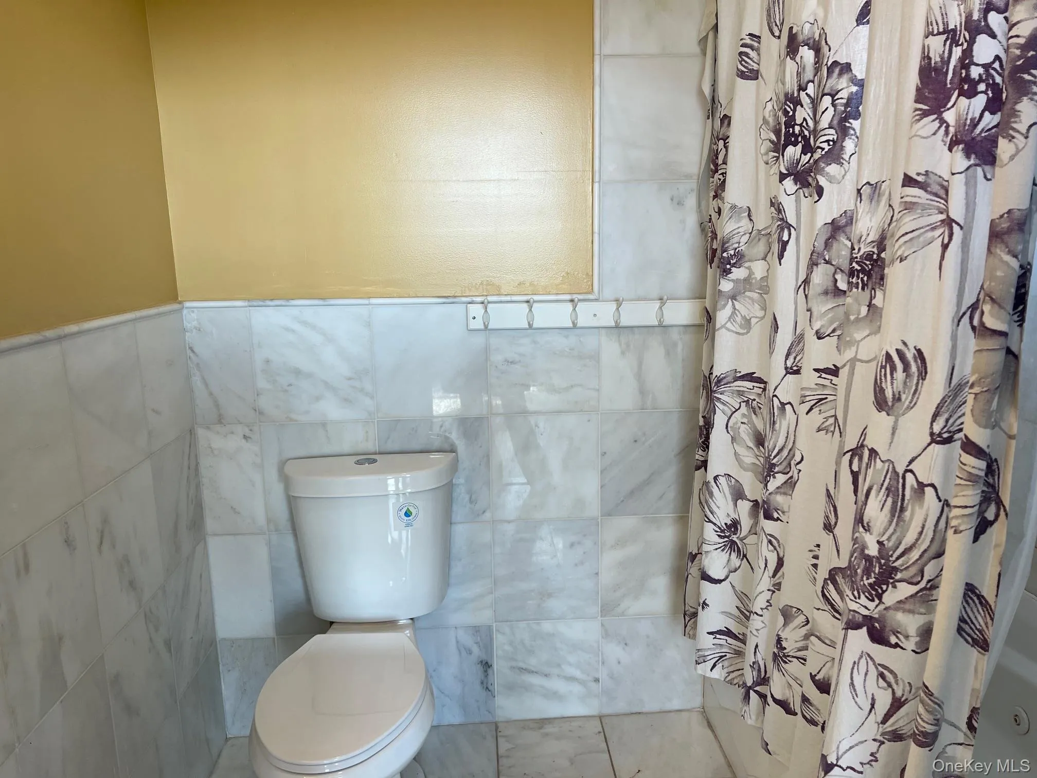 Bathroom featuring toilet, a shower with shower curtain, and tile walls Bathroom featuring toilet, a shower with shower curtain, and tile walls