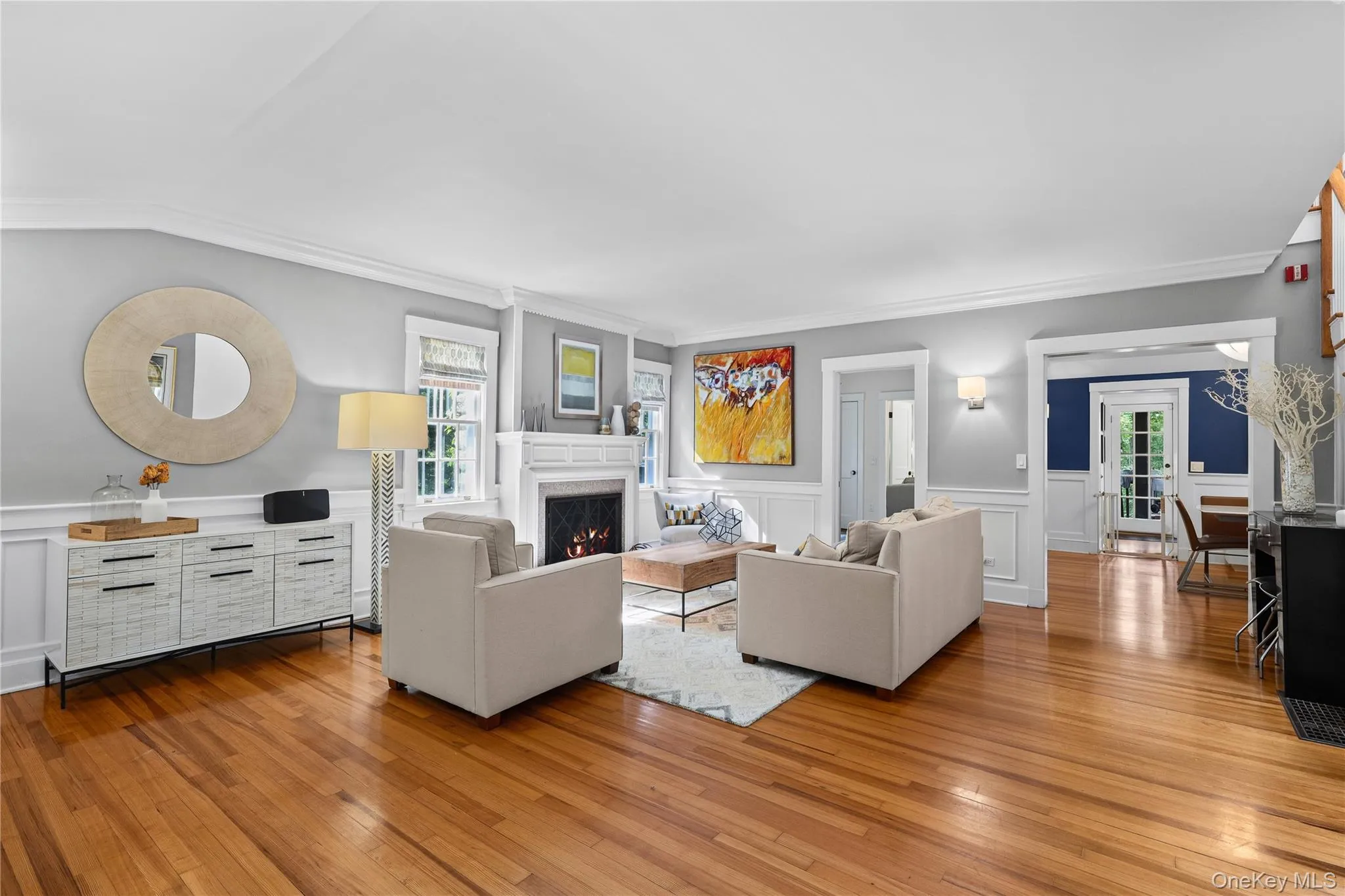 Spacious Living room featuring wood-finished flooring, white wainscoting, and a traditional fireplace. Spacious Living room featuring wood-finished flooring, white wainscoting, and a traditional fireplace.