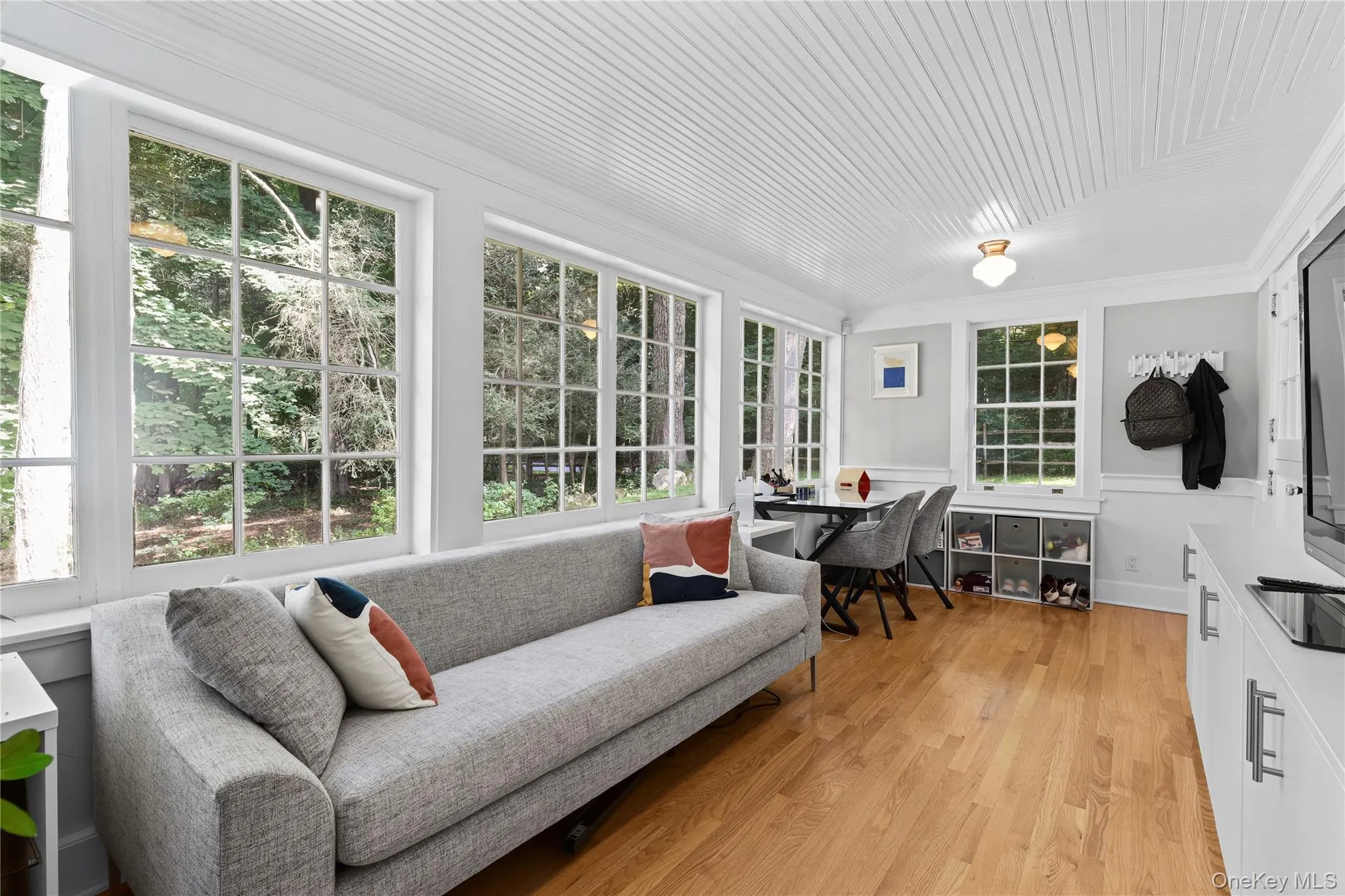 Sun room featuring wood-finish flooring, beadboard ceiling, and multiple grid-pattern windows, and built-ins. Sun room featuring wood-finish flooring, beadboard ceiling, and multiple grid-pattern windows, and built-ins.