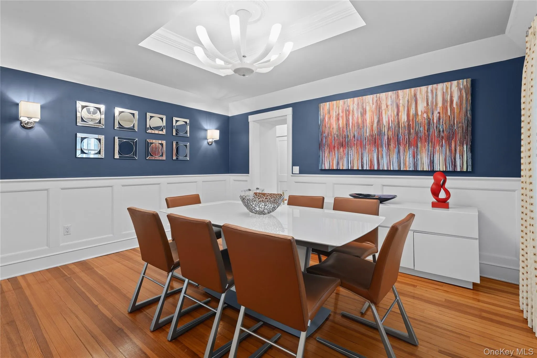 Dining room featuring wood-finish flooring, white wainscoting, and a tray ceiling. Dining room featuring wood-finish flooring, white wainscoting, and a tray ceiling.