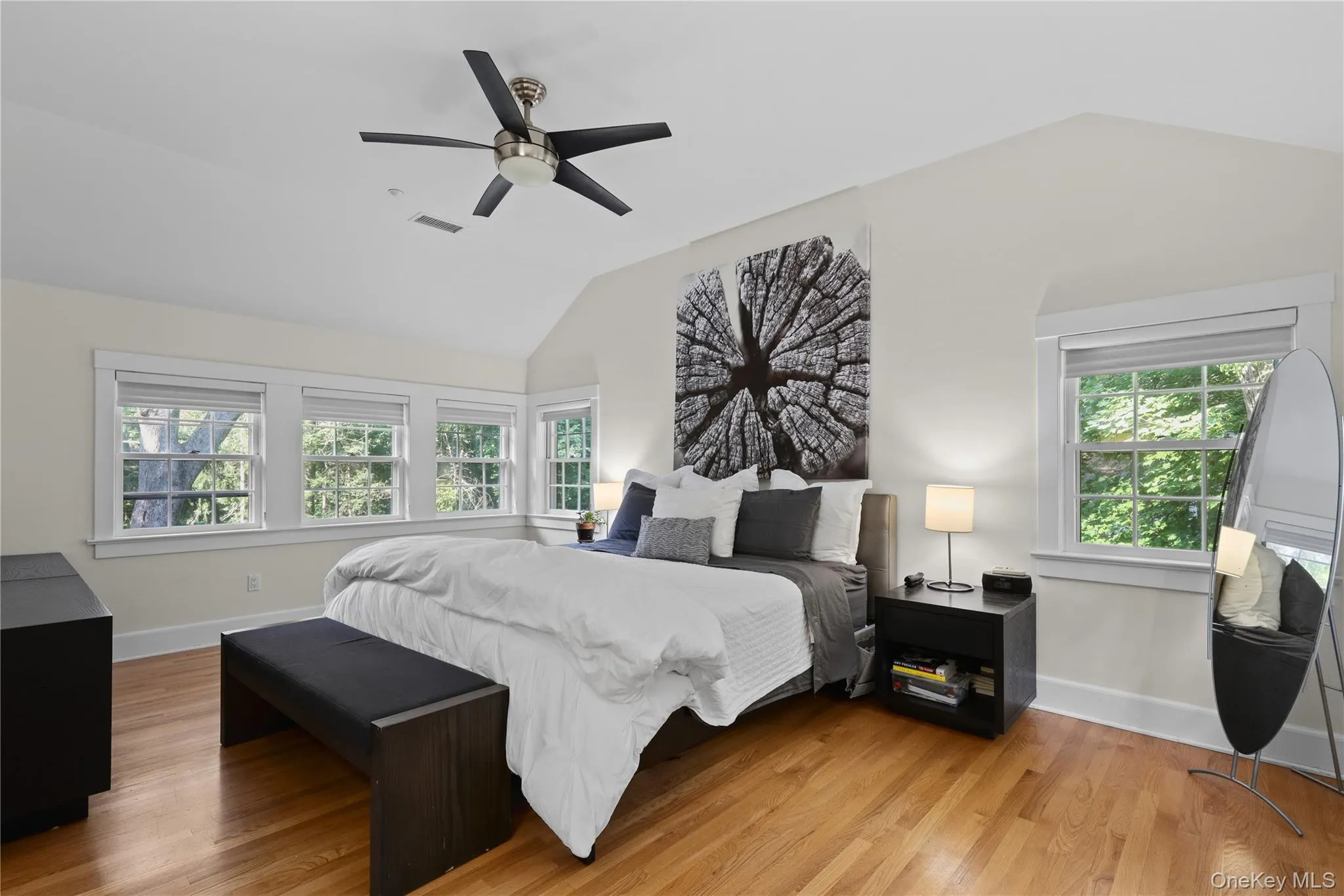 Primary Bedroom featuring vaulted ceilings, a ceiling fan, wood-finish flooring, and multiple windows. Primary Bedroom featuring vaulted ceilings, a ceiling fan, wood-finish flooring, and multiple windows.