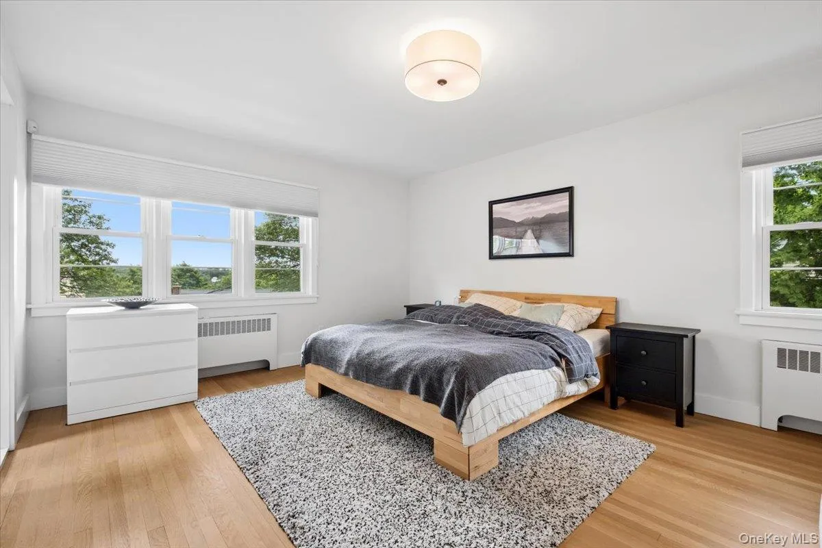 Bright bedroom featuring hard wood flooring, white walls, and a large triple window with white trim Bright bedroom featuring hard wood flooring, white walls, and a large triple window with white trim