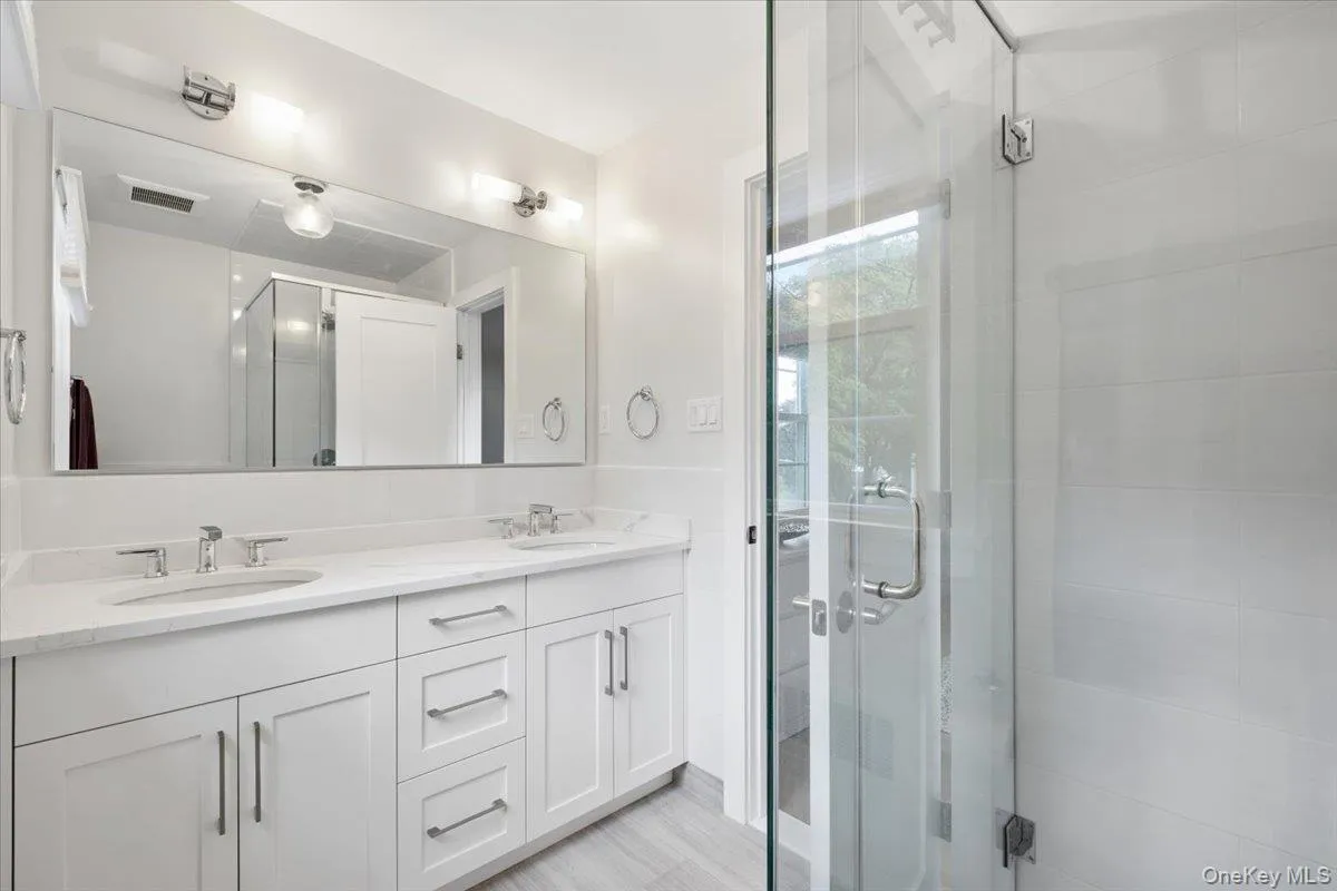 Modern bathroom featuring a dual vanity with white shaker-style cabinetry, chrome hardware, and a stylish quartz countertop Modern bathroom featuring a dual vanity with white shaker-style cabinetry, chrome hardware, and a stylish quartz countertop