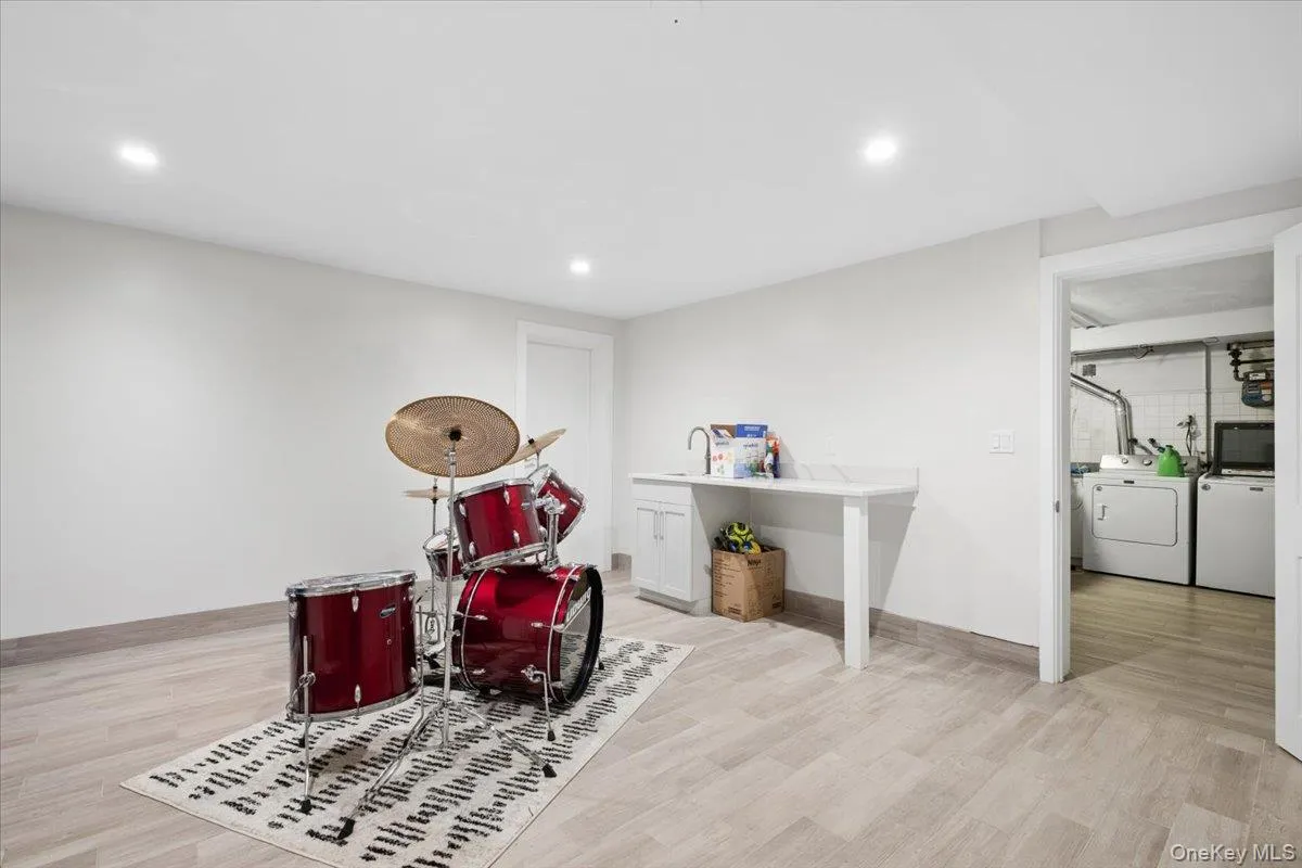 Finished basement/play area space featuring light-toned wood-finish flooring, recessed lighting, and a built-in wet bar with a white quartz countertop Finished basement/play area space featuring light-toned wood-finish flooring, recessed lighting, and a built-in wet bar with a white quartz countertop