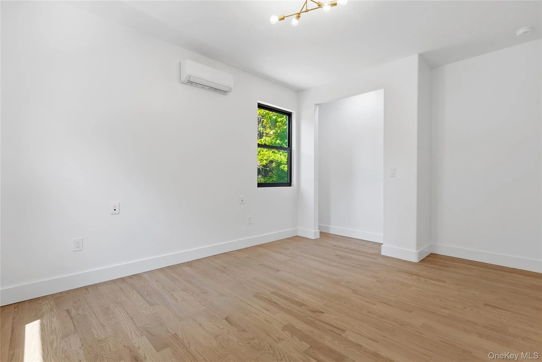 Spacious room featuring wood-finish flooring and a contemporary chandelier Spacious room featuring wood-finish flooring and a contemporary chandelier