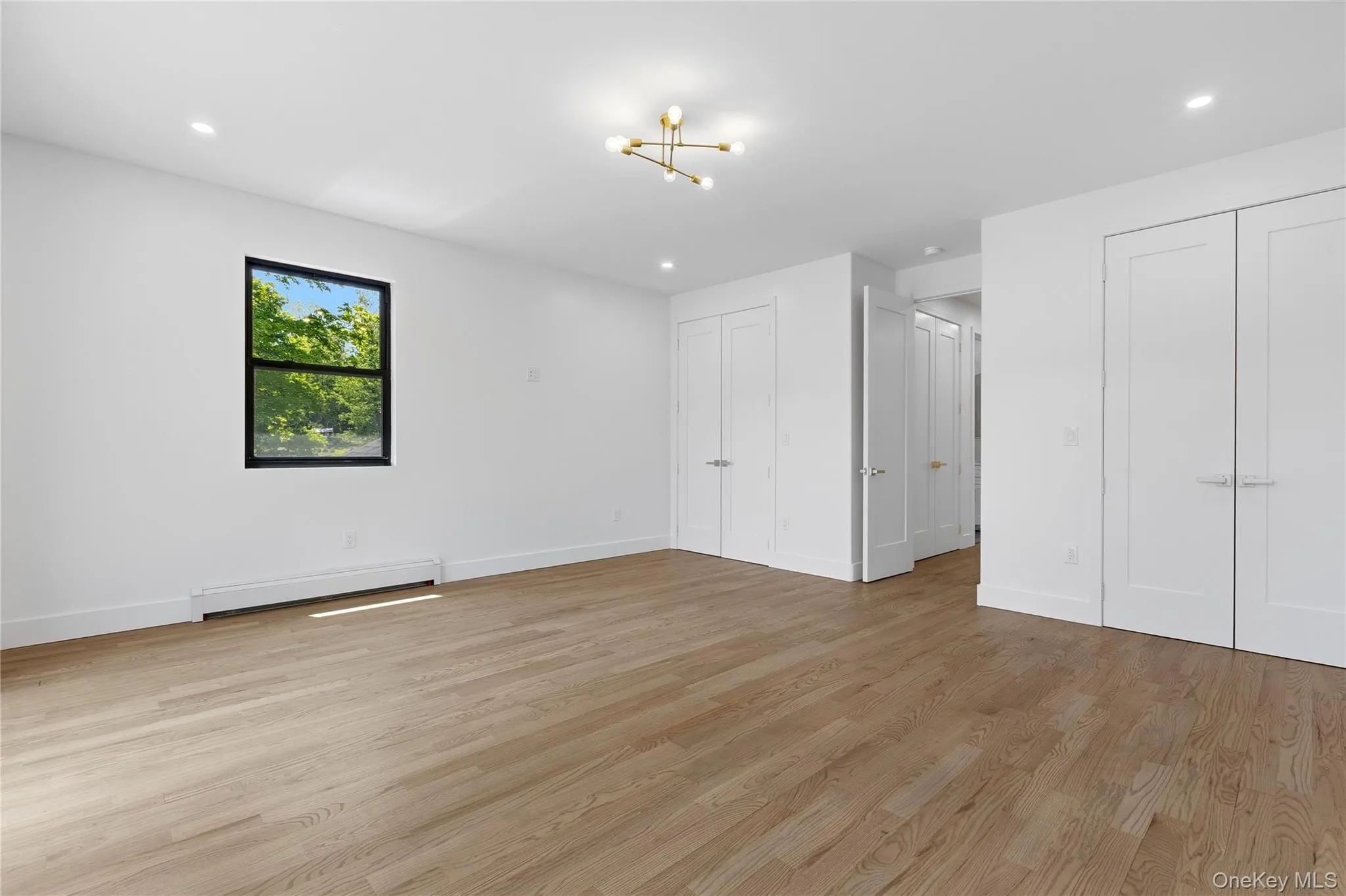 Spacious room featuring light wood-finish flooring, white walls, and a contemporary ceiling fixture Spacious room featuring light wood-finish flooring, white walls, and a contemporary ceiling fixture