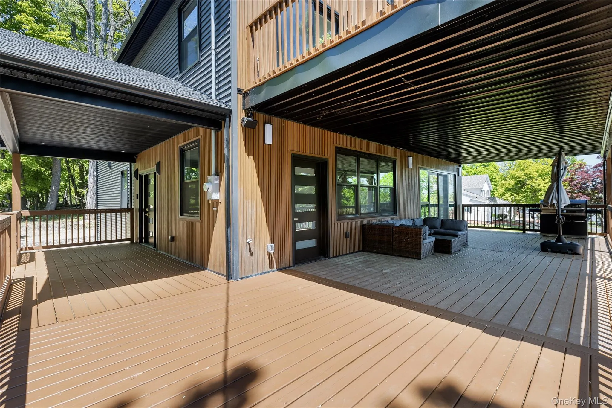 Expansive outdoor decking featuring a covered patio, wood-finish siding, and a contemporary glass-paneled entry door Expansive outdoor decking featuring a covered patio, wood-finish siding, and a contemporary glass-paneled entry door