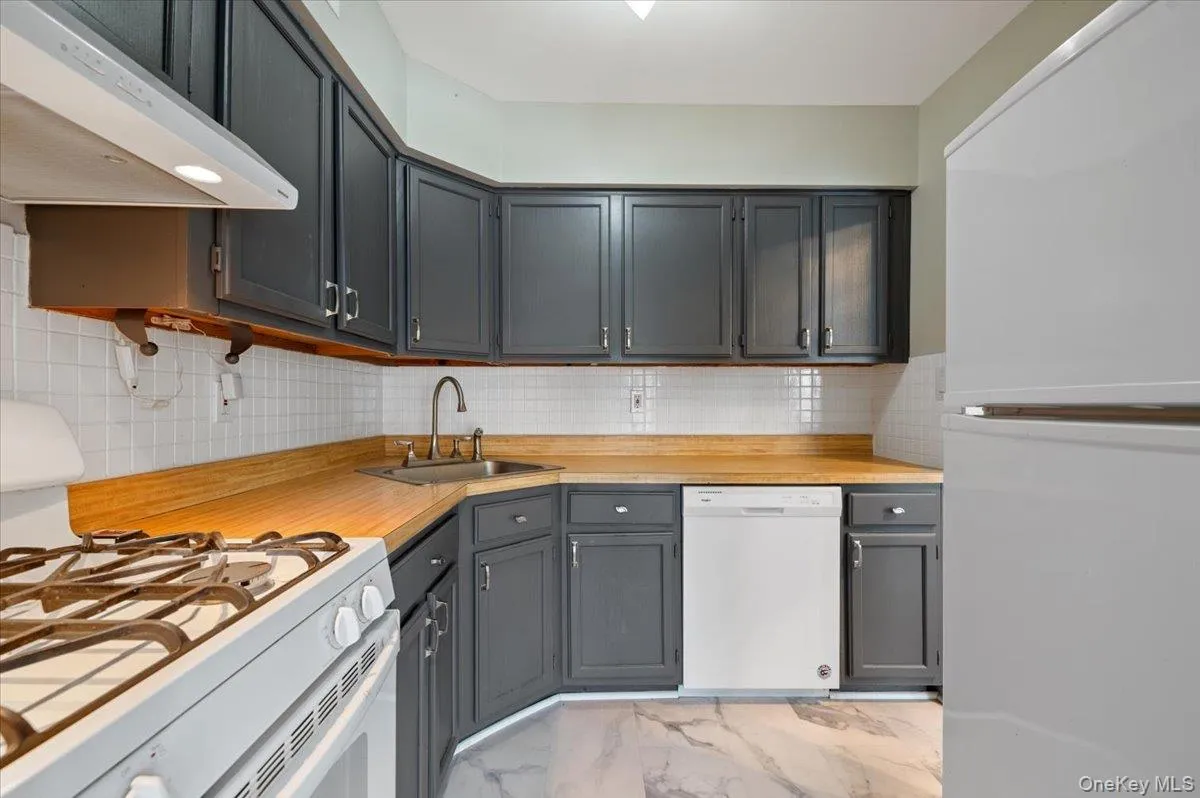 Kitchen featuring charcoal-painted cabinetry, wood-finish countertops, and a white subway tile backsplash Kitchen featuring charcoal-painted cabinetry, wood-finish countertops, and a white subway tile backsplash