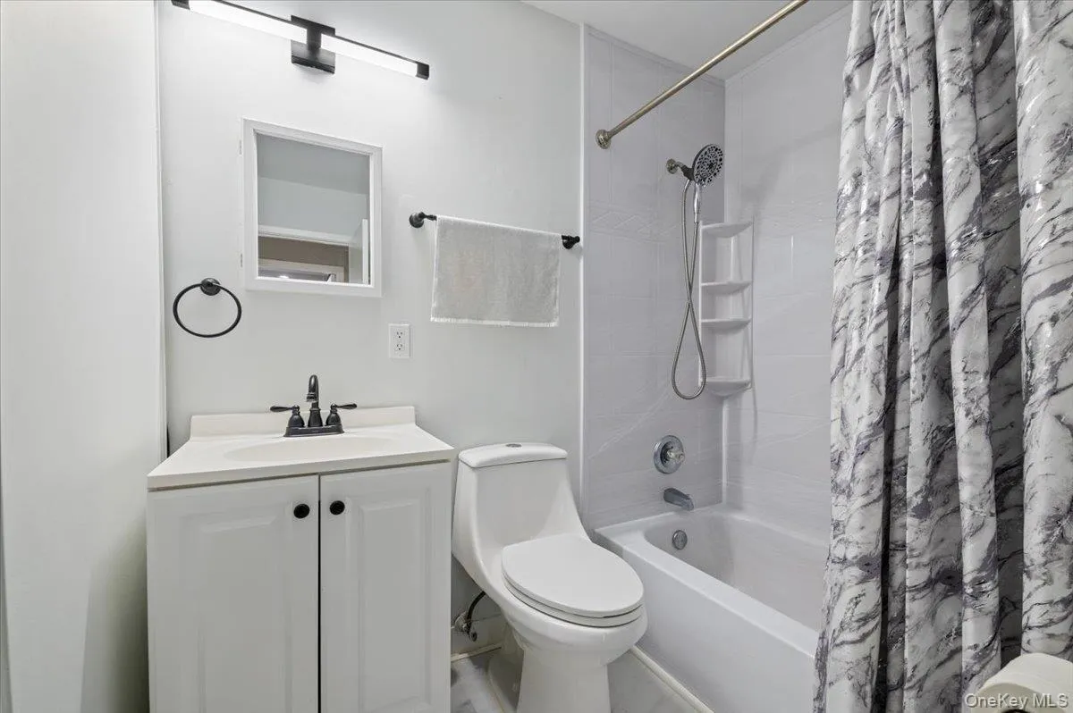 Updated bathroom featuring a white vanity with black hardware, a rectangular vanity mirror, and a modern black wall-mounted light fixture Updated bathroom featuring a white vanity with black hardware, a rectangular vanity mirror, and a modern black wall-mounted light fixture