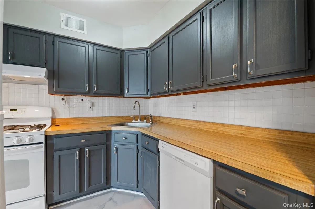 Kitchen featuring dark gray cabinetry with silver hardware, wood-finish countertops, white subway tile backsplash, and a corner sink with a gooseneck faucet Kitchen featuring dark gray cabinetry with silver hardware, wood-finish countertops, white subway tile backsplash, and a corner sink with a gooseneck faucet