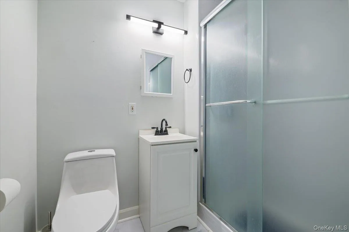 Bathroom featuring a white vanity with a dark faucet, a white toilet, and a frosted glass shower enclosure Bathroom featuring a white vanity with a dark faucet, a white toilet, and a frosted glass shower enclosure