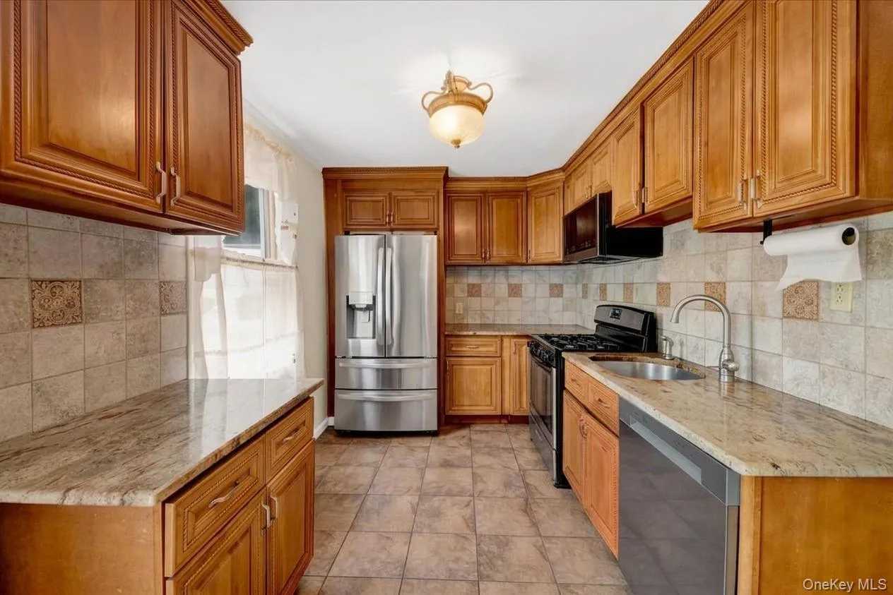 Kitchen featuring wood cabinetry, stainless steel appliances, tile flooring, stone countertops, and a tile backsplash Kitchen featuring wood cabinetry, stainless steel appliances, tile flooring, stone countertops, and a tile backsplash