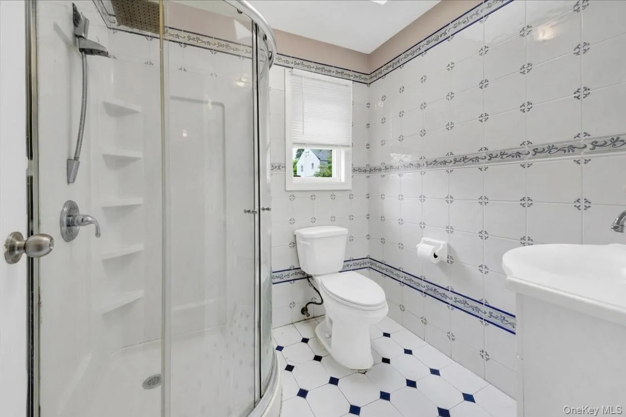 2nd floor full bathroom featuring a glass-enclosed shower, white vanity sink, white toilet, patterned floor tiles, and decorative wall tiles 2nd floor full bathroom featuring a glass-enclosed shower, white vanity sink, white toilet, patterned floor tiles, and decorative wall tiles