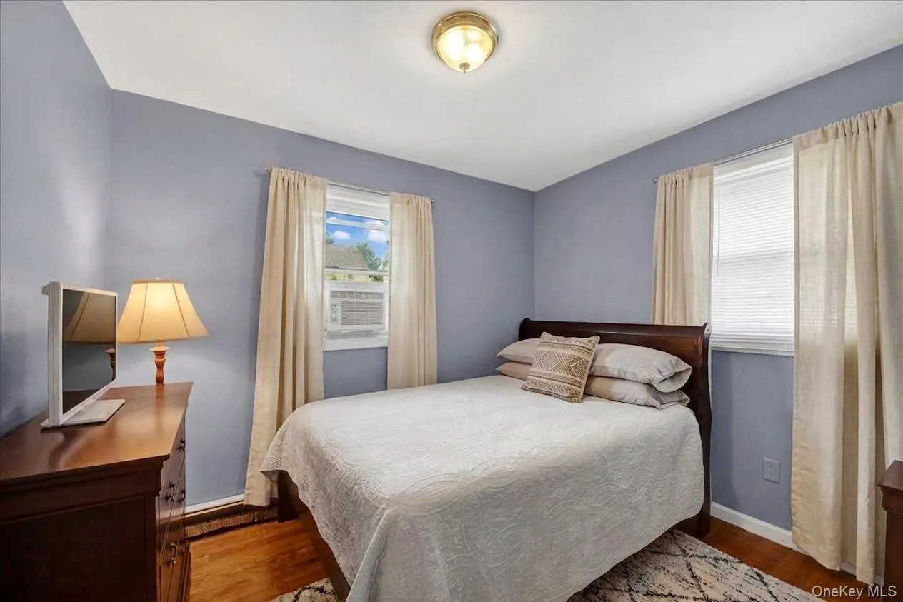 3rd bedroom featuring light blue walls, hardwood flooring, and a window with blinds and drapes 3rd bedroom featuring light blue walls, hardwood flooring, and a window with blinds and drapes