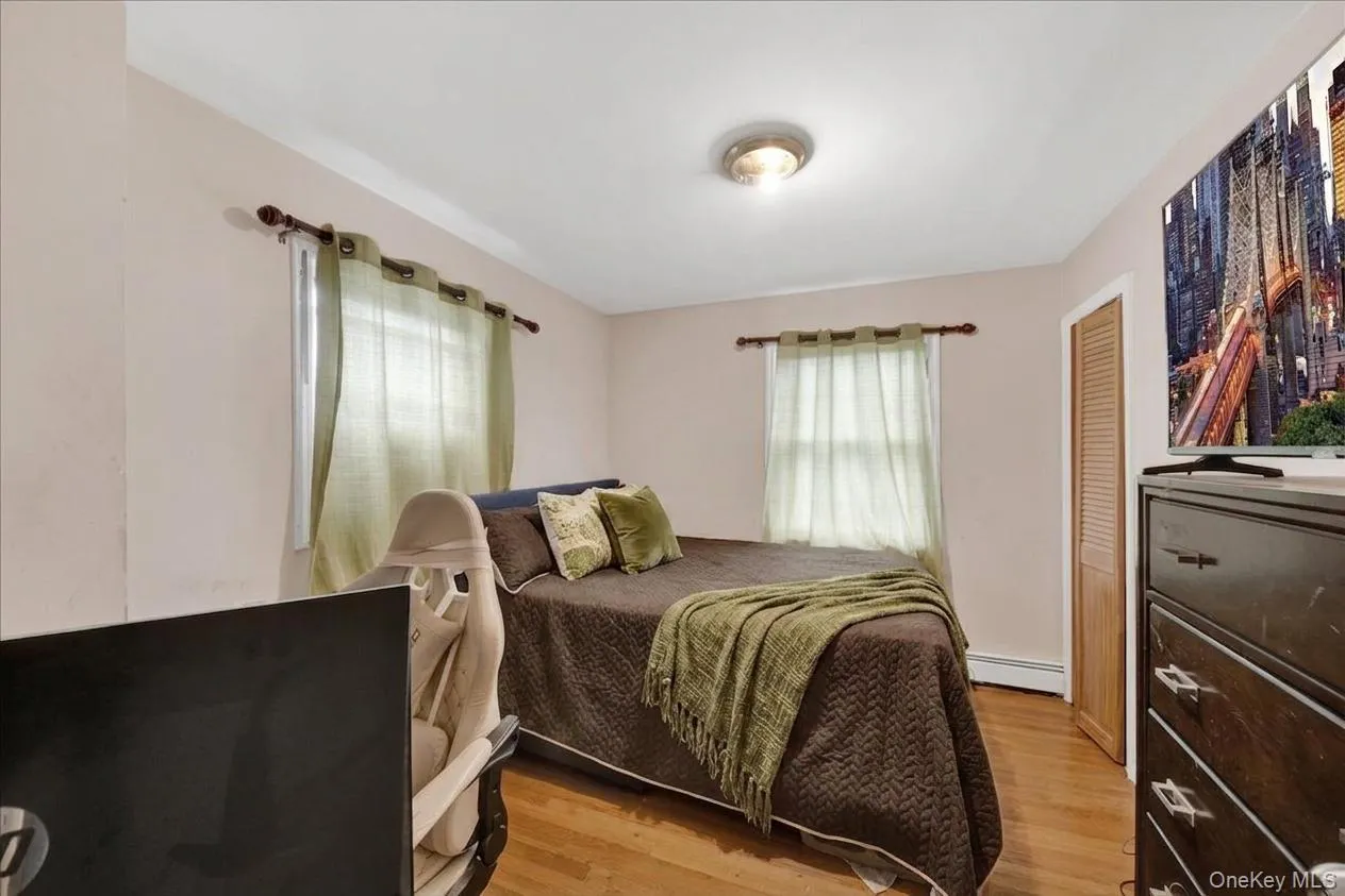 4th bedroom featuring wood-finish flooring, two windows with curtain rods, a ceiling-mounted light fixture, and a louvered bi-fold door 4th bedroom featuring wood-finish flooring, two windows with curtain rods, a ceiling-mounted light fixture, and a louvered bi-fold door