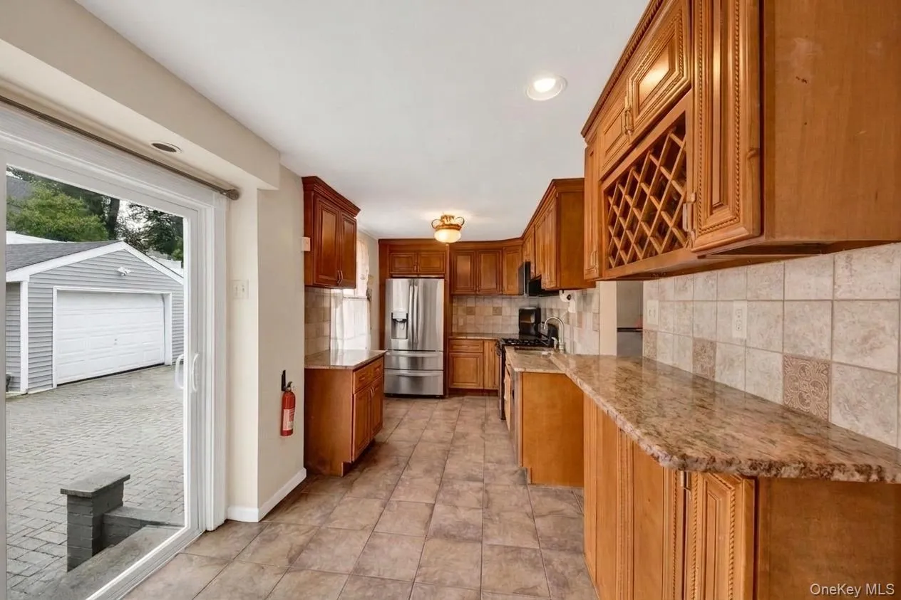 Kitchen featuring wood cabinetry, granite-look countertops, tiled backsplash, and stainless steel appliances Kitchen featuring wood cabinetry, granite-look countertops, tiled backsplash, and stainless steel appliances