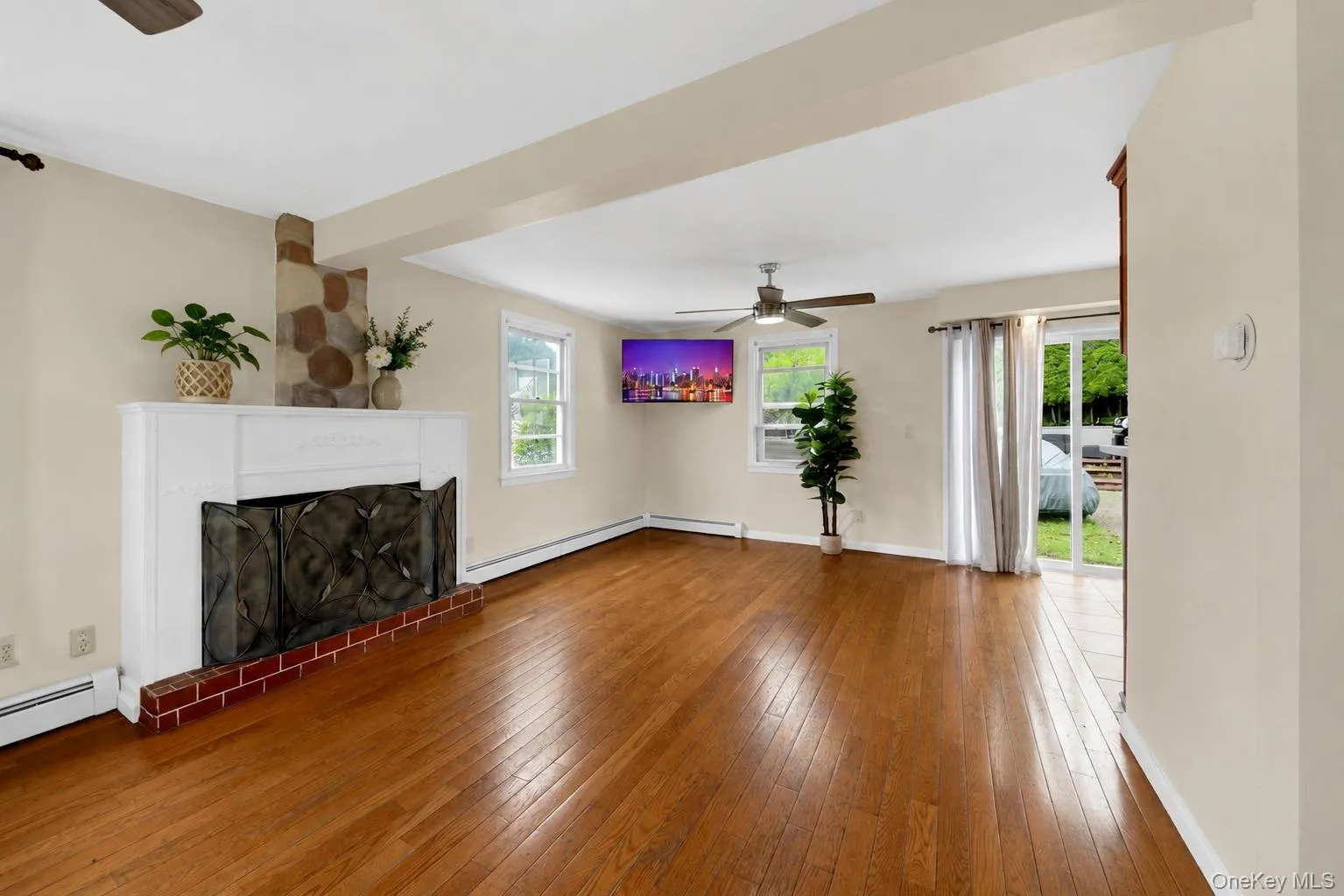 Spacious interior featuring wood-finish flooring, a stone fireplace with a white mantel, and a ceiling fan Spacious interior featuring wood-finish flooring, a stone fireplace with a white mantel, and a ceiling fan