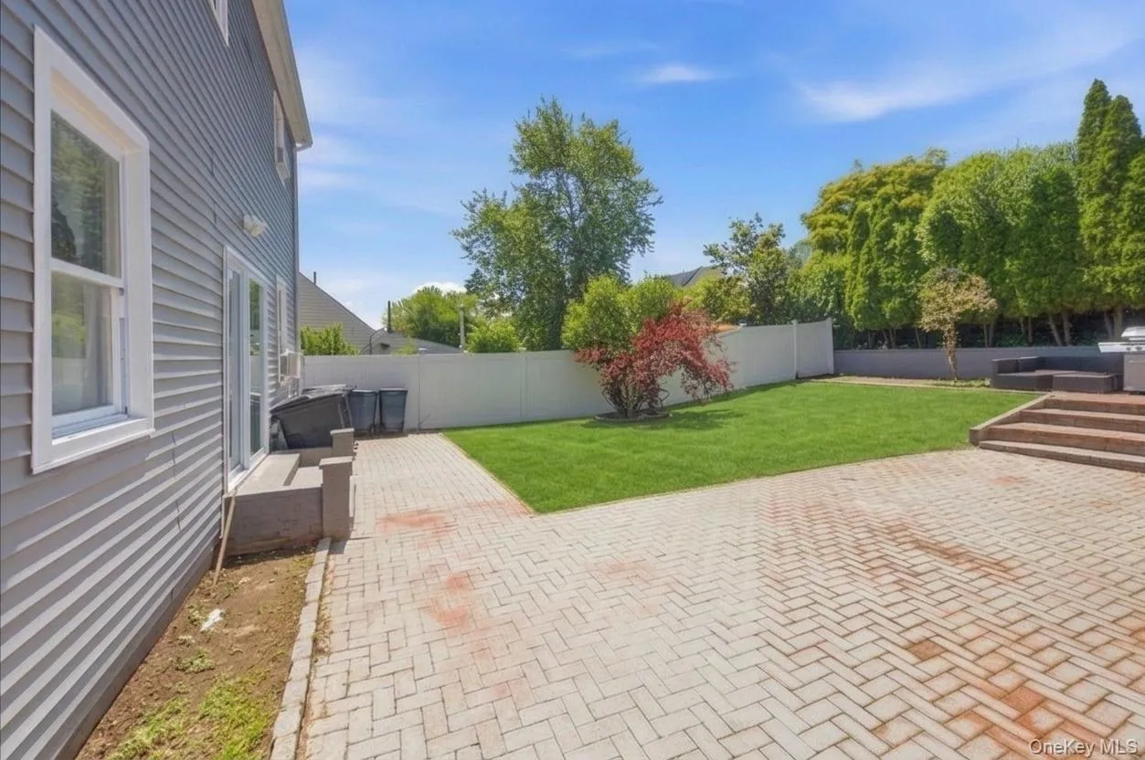 Expansive paver patio with a manicured lawn, white privacy fencing, and mature perimeter trees Expansive paver patio with a manicured lawn, white privacy fencing, and mature perimeter trees