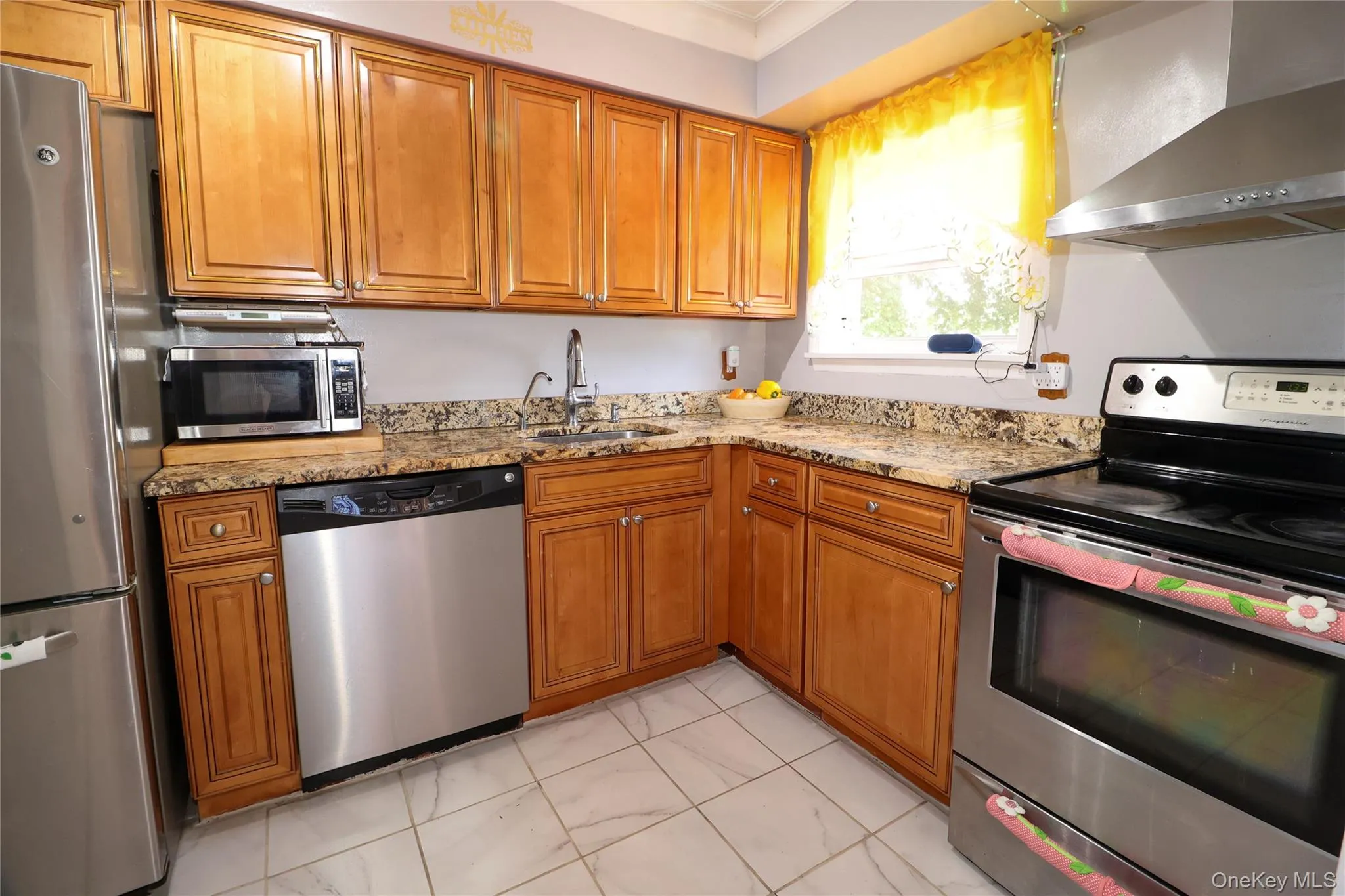 Kitchen featuring wood-finish cabinetry, granite-style countertops, stainless steel appliances, a corner sink with a gooseneck faucet, and tile flooring Kitchen featuring wood-finish cabinetry, granite-style countertops, stainless steel appliances, a corner sink with a gooseneck faucet, and tile flooring