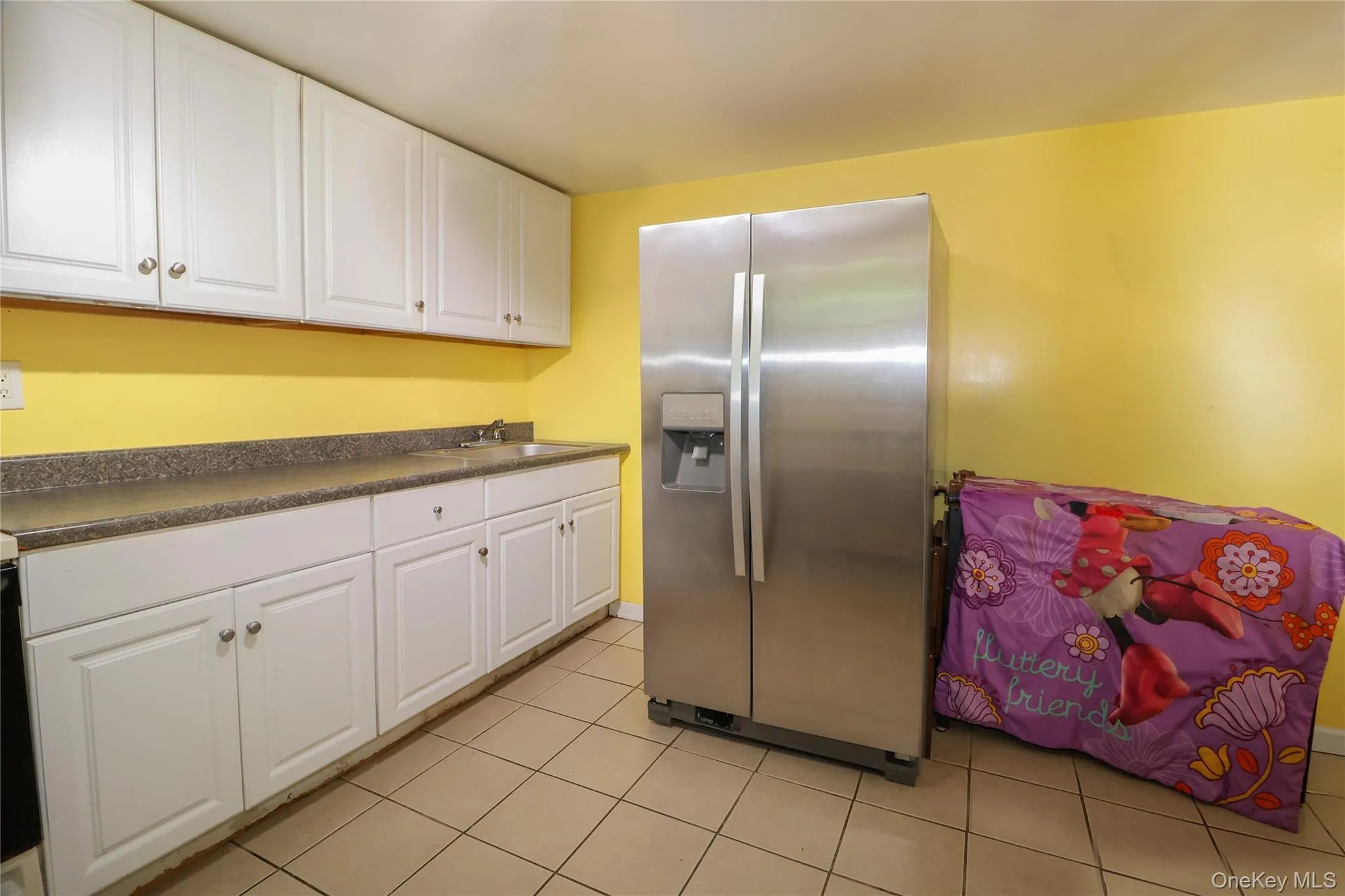 Kitchen featuring white cabinetry, gray speckled countertops, a stainless steel refrigerator, and tiled flooring Kitchen featuring white cabinetry, gray speckled countertops, a stainless steel refrigerator, and tiled flooring