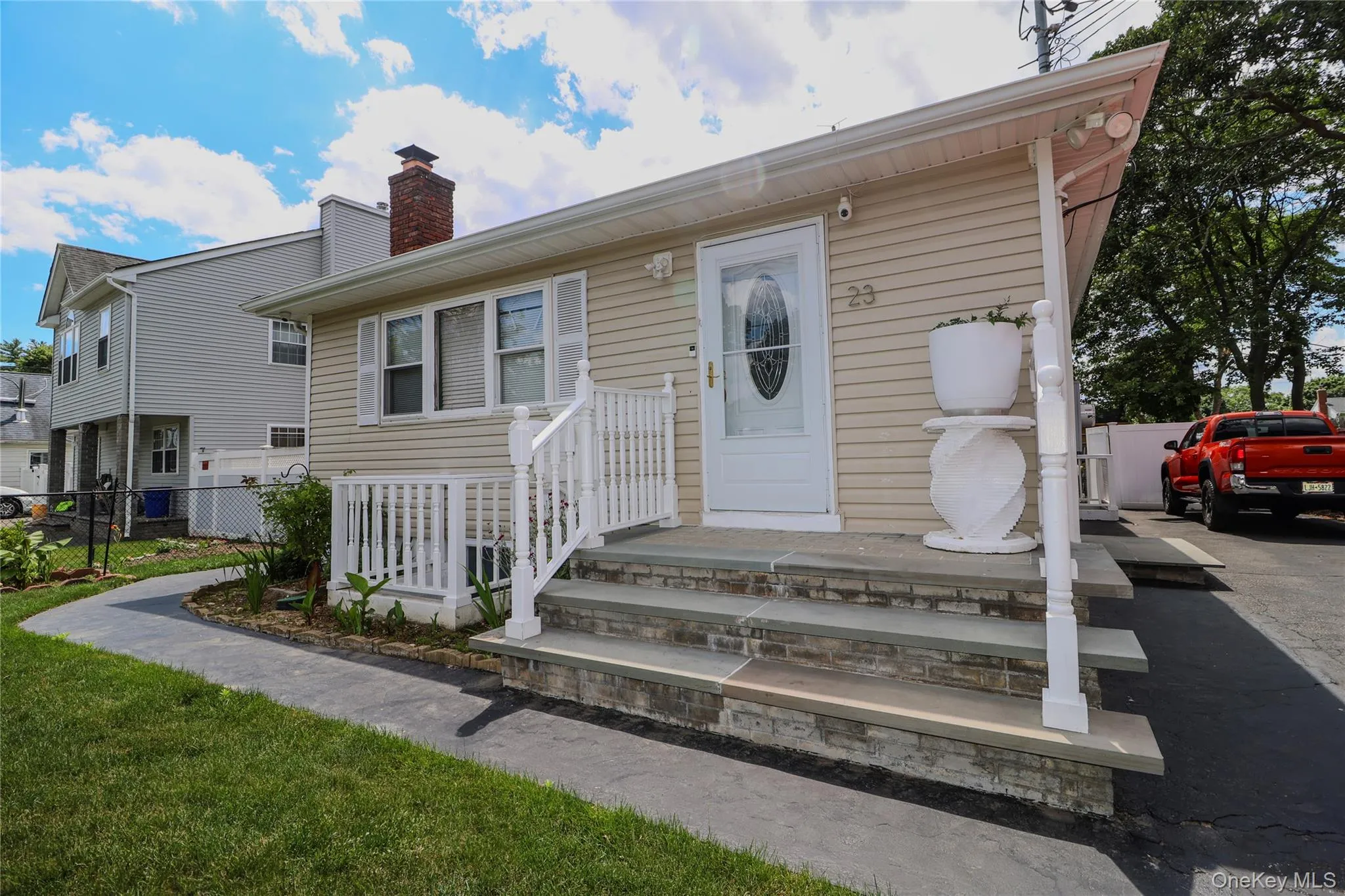Exterior featuring light beige siding, a stone-faced porch with white railings, and a paved driveway Exterior featuring light beige siding, a stone-faced porch with white railings, and a paved driveway