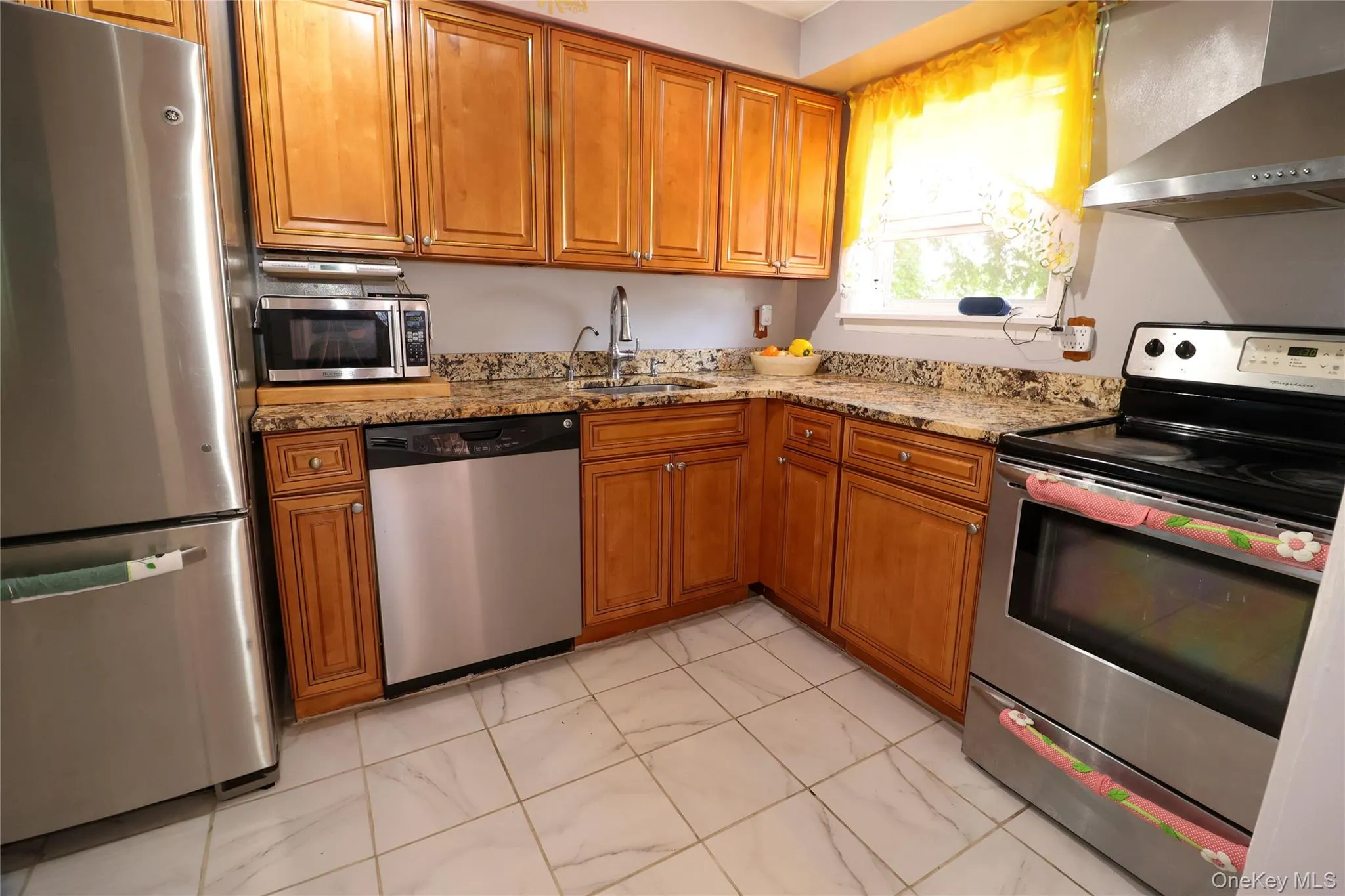 Kitchen featuring wood cabinetry, granite-style countertops, stainless steel appliances, and tile flooring Kitchen featuring wood cabinetry, granite-style countertops, stainless steel appliances, and tile flooring