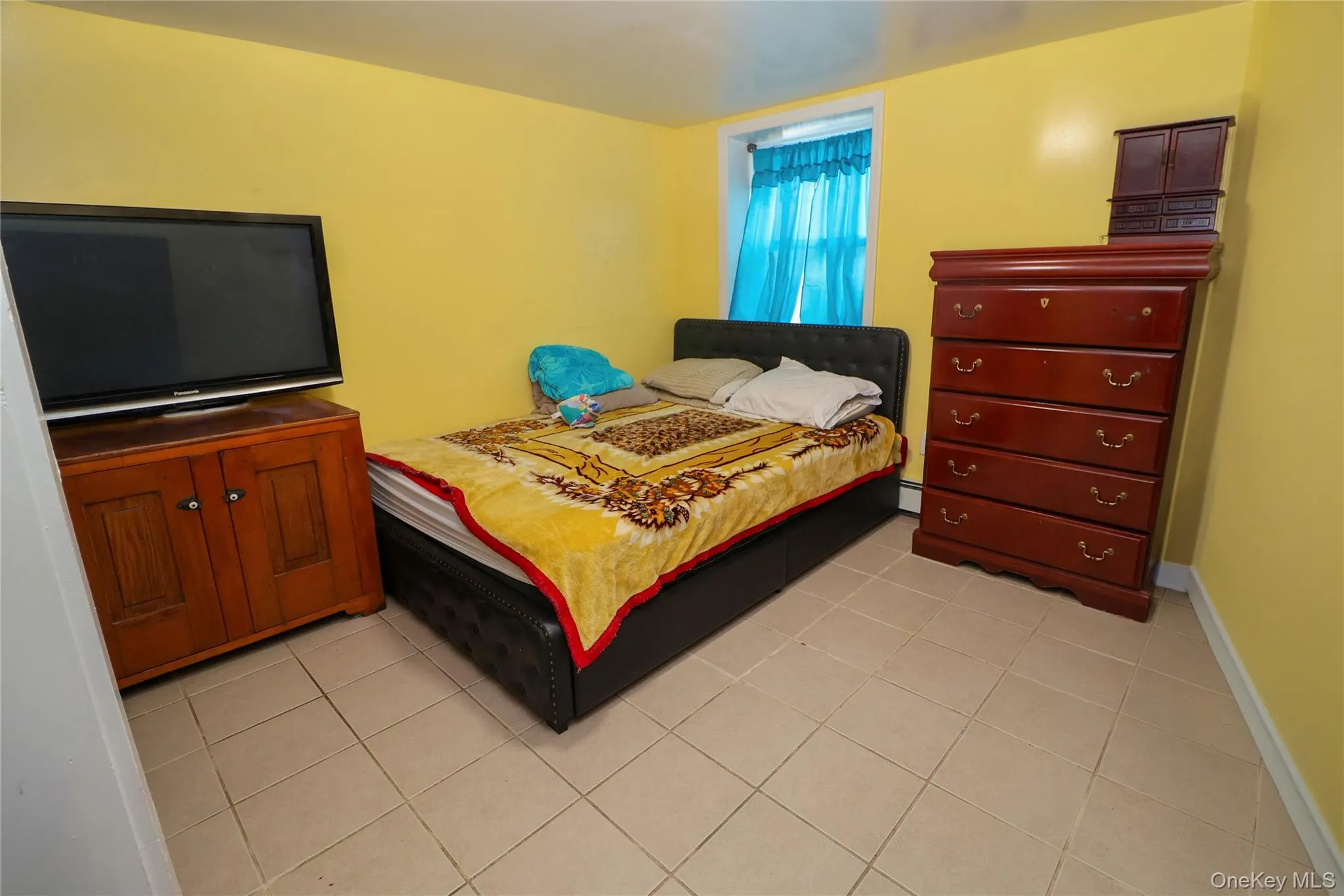 Neutral-toned tile flooring extends throughout this room, featuring vibrant yellow walls and a window with blue curtains Neutral-toned tile flooring extends throughout this room, featuring vibrant yellow walls and a window with blue curtains