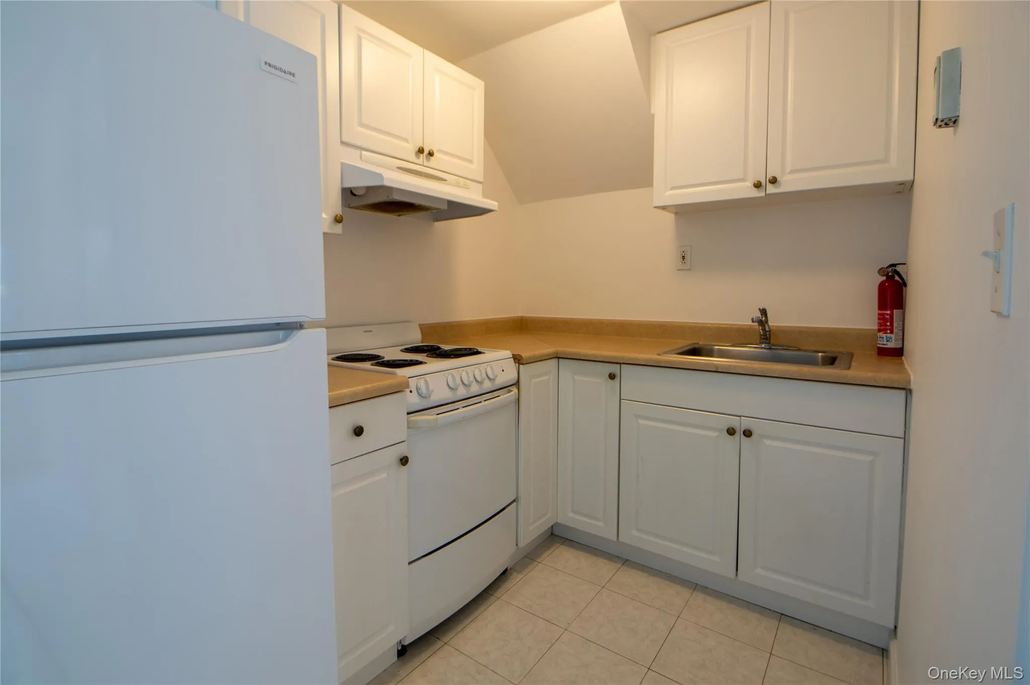 Kitchen featuring light tile patterned floors, a sink, white appliances, under cabinet range hood, and white cabinetry Kitchen featuring light tile patterned floors, a sink, white appliances, under cabinet range hood, and white cabinetry