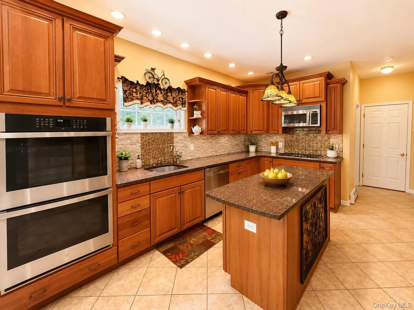 Kitchen featuring wood cabinetry, stainless steel double wall ovens, a central island with a granite-style countertop, a tile backsplash, and recessed lighting Kitchen featuring wood cabinetry, stainless steel double wall ovens, a central island with a granite-style countertop, a tile backsplash, and recessed lighting