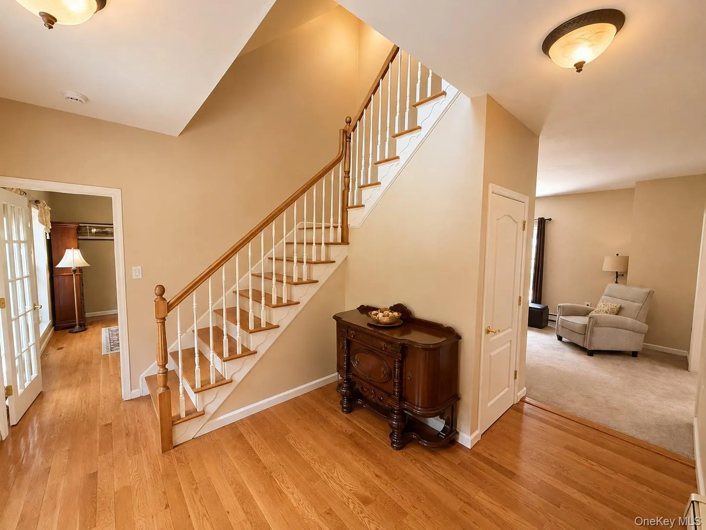 Open foyer featuring wood-finish flooring and a staircase with white risers and a wood-finish handrail Open foyer featuring wood-finish flooring and a staircase with white risers and a wood-finish handrail