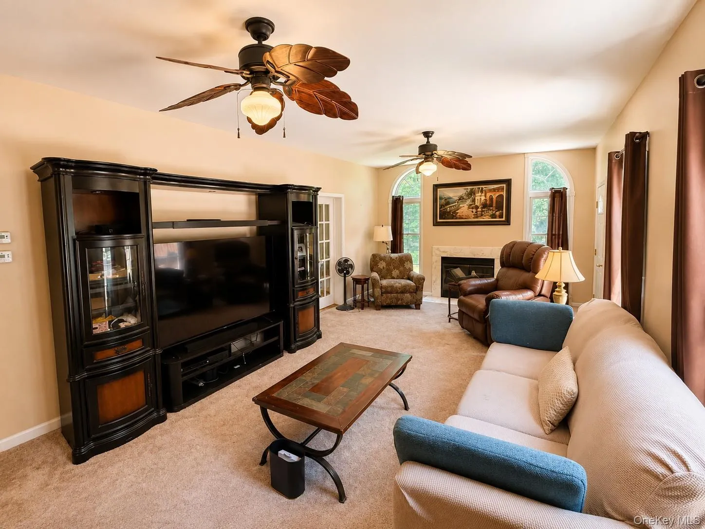 Spacious living area featuring neutral carpeting, a fireplace with a stone surround, and multiple arched windows Spacious living area featuring neutral carpeting, a fireplace with a stone surround, and multiple arched windows