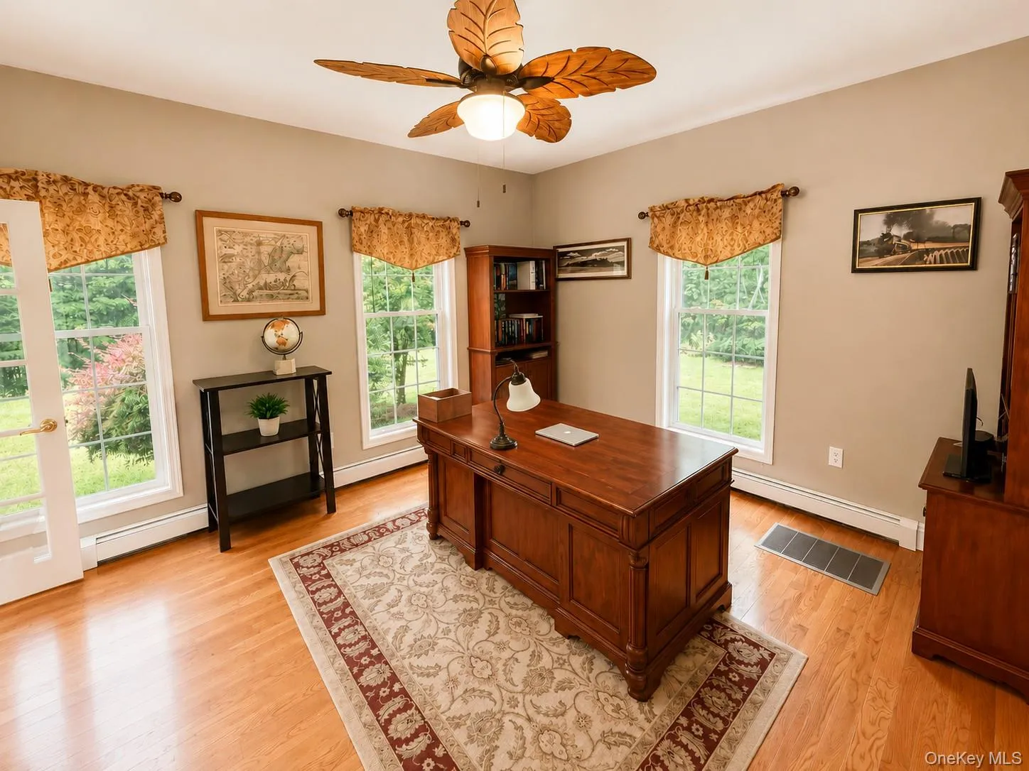 Bright interior room featuring wood-finish flooring, light tan wall color, and multiple windows with white trim Bright interior room featuring wood-finish flooring, light tan wall color, and multiple windows with white trim