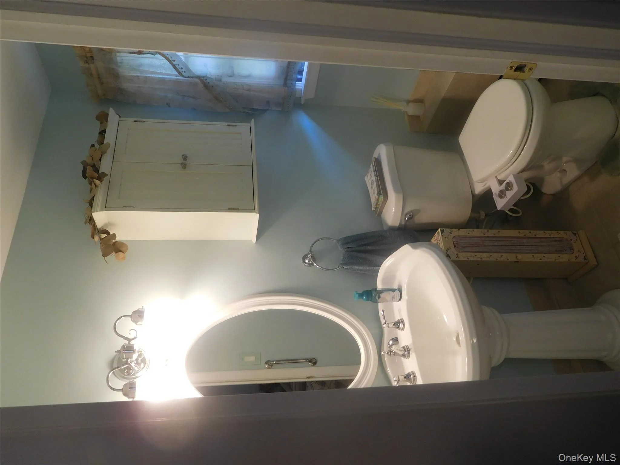 Pedestal sink with chrome fixtures and an oval mirror, complemented by a wall-mounted cabinet and a toilet Pedestal sink with chrome fixtures and an oval mirror, complemented by a wall-mounted cabinet and a toilet
