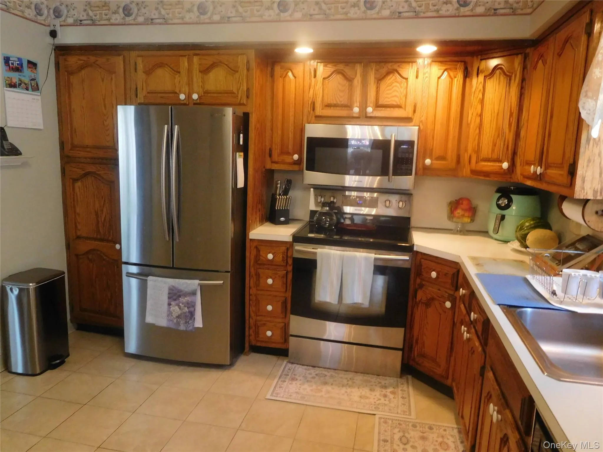 Kitchen featuring wood cabinetry, stainless steel appliances, and light-toned tile flooring Kitchen featuring wood cabinetry, stainless steel appliances, and light-toned tile flooring