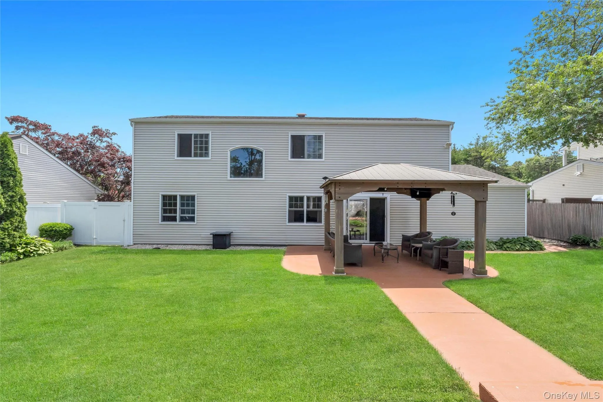 Expansive backyard featuring a manicured lawn, a paved patio with a gazebo, and a rear exterior with siding Expansive backyard featuring a manicured lawn, a paved patio with a gazebo, and a rear exterior with siding