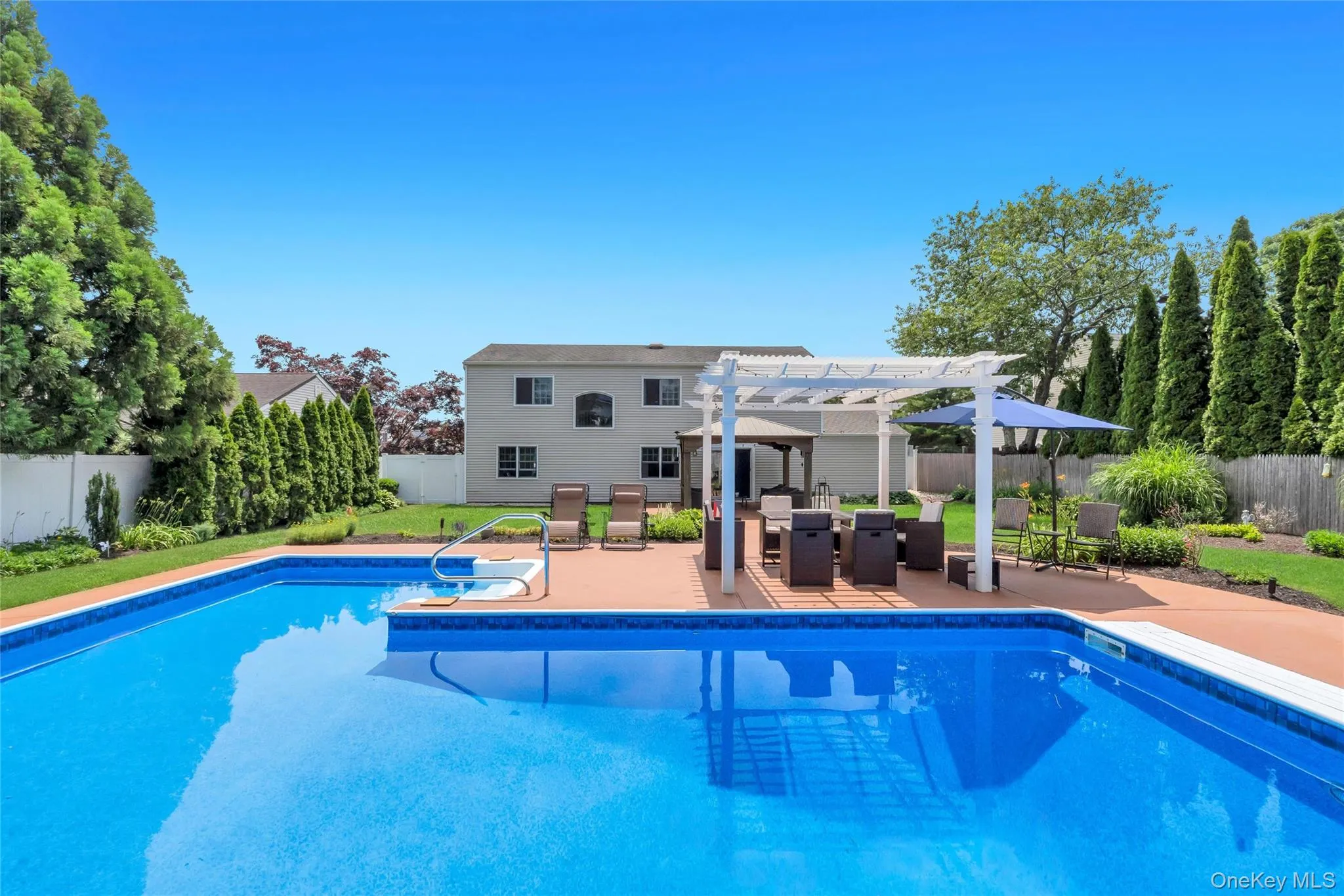 Expansive backyard featuring an in-ground pool with an integrated spa, a large patio area, and a white pergola Expansive backyard featuring an in-ground pool with an integrated spa, a large patio area, and a white pergola