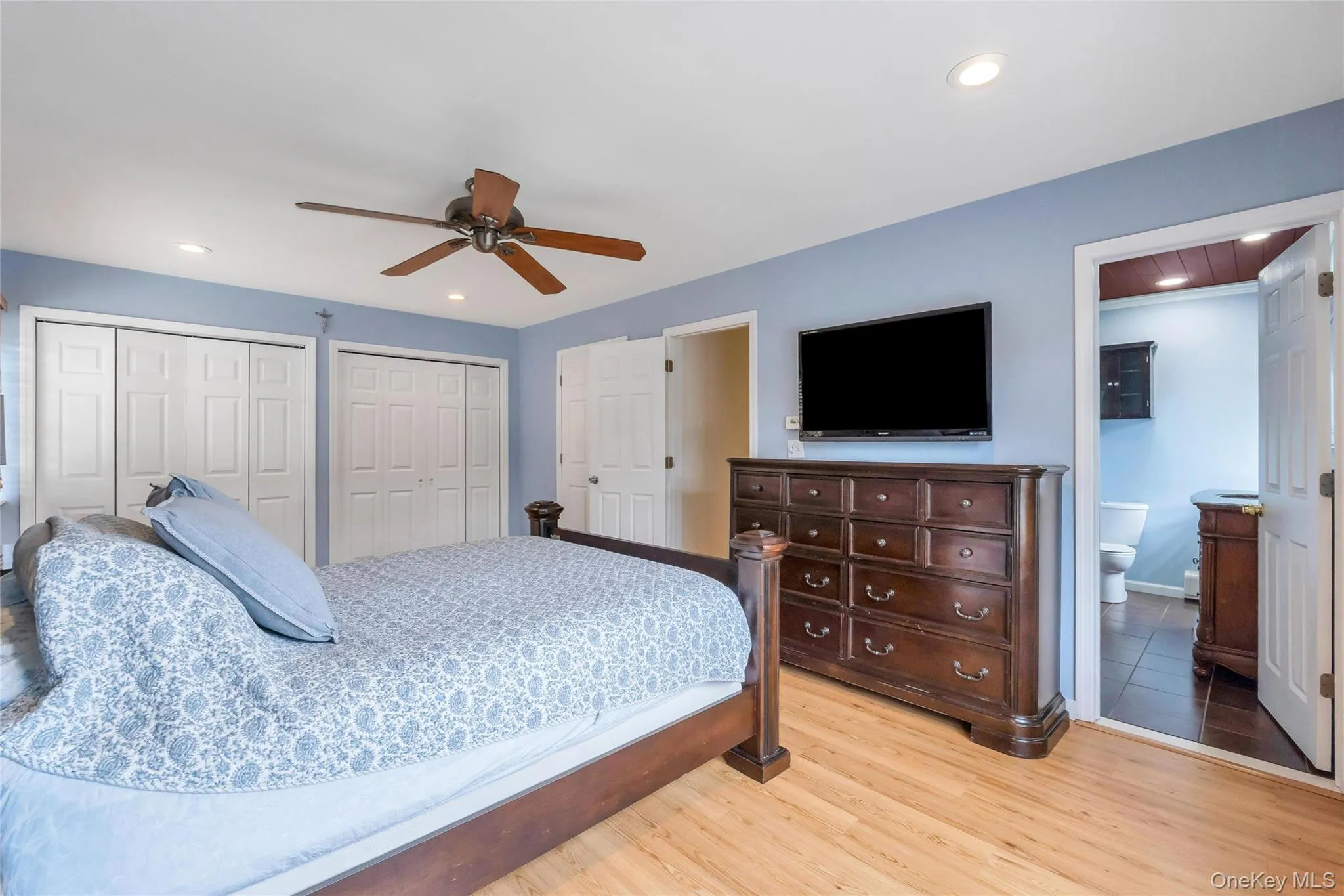 Room featuring light wood-finish flooring, two sets of white bifold closet doors, recessed ceiling lighting, and a ceiling fan with wood-tone blades Room featuring light wood-finish flooring, two sets of white bifold closet doors, recessed ceiling lighting, and a ceiling fan with wood-tone blades