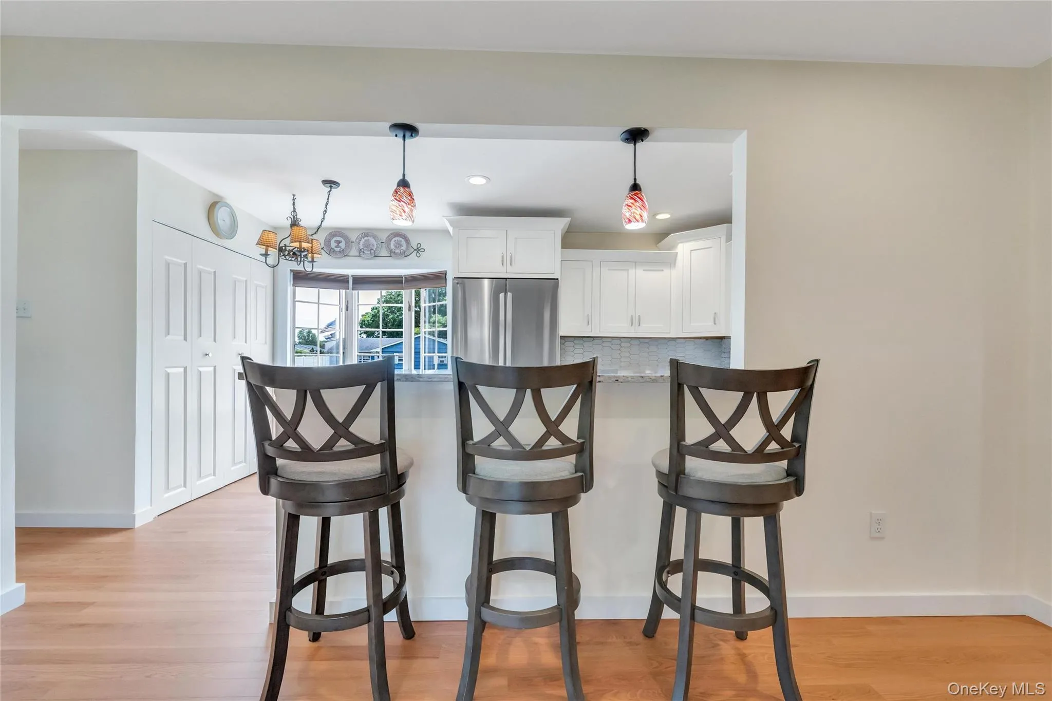Kitchen pass-through featuring an extended countertop, two pendant lights, and a stone backsplash Kitchen pass-through featuring an extended countertop, two pendant lights, and a stone backsplash