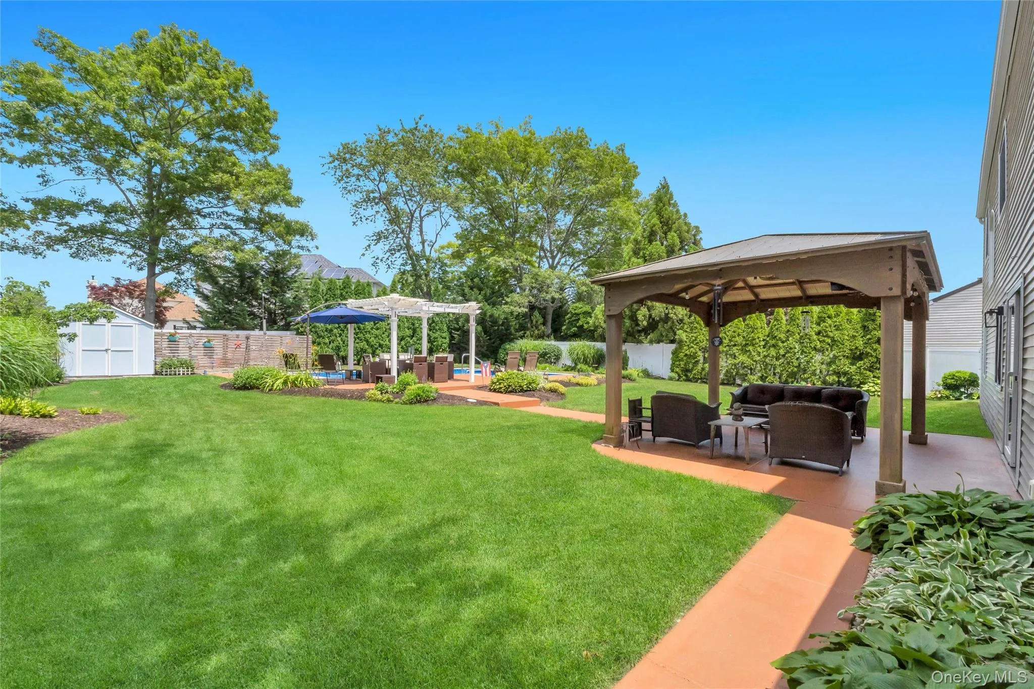 Expansive backyard featuring a lush lawn, a covered patio area with a gazebo, and a secondary paved patio with a pergola Expansive backyard featuring a lush lawn, a covered patio area with a gazebo, and a secondary paved patio with a pergola