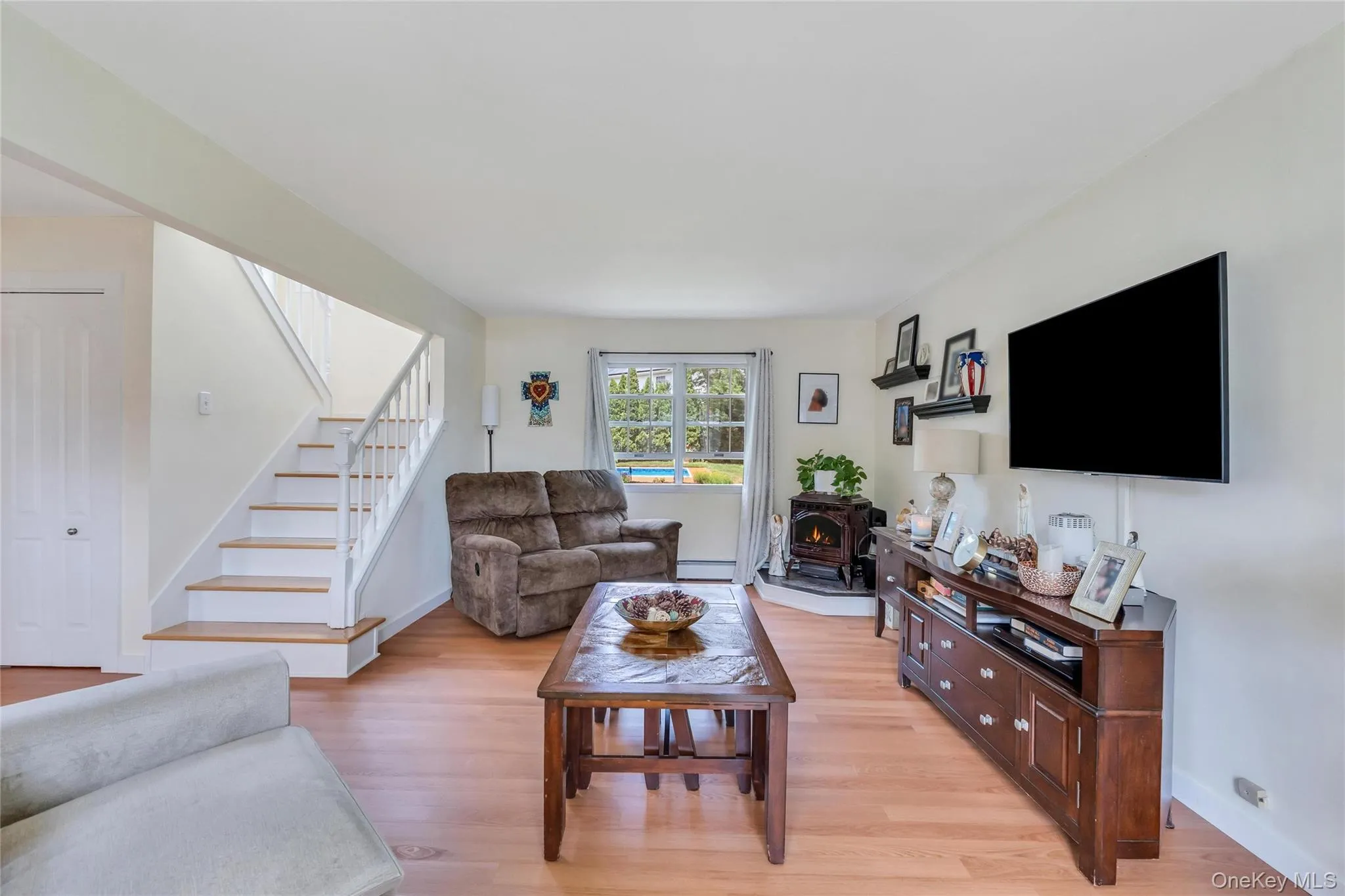 Open living area featuring wood-finish flooring, a built-in wood-burning stove, and a staircase with white risers and wood treads Open living area featuring wood-finish flooring, a built-in wood-burning stove, and a staircase with white risers and wood treads