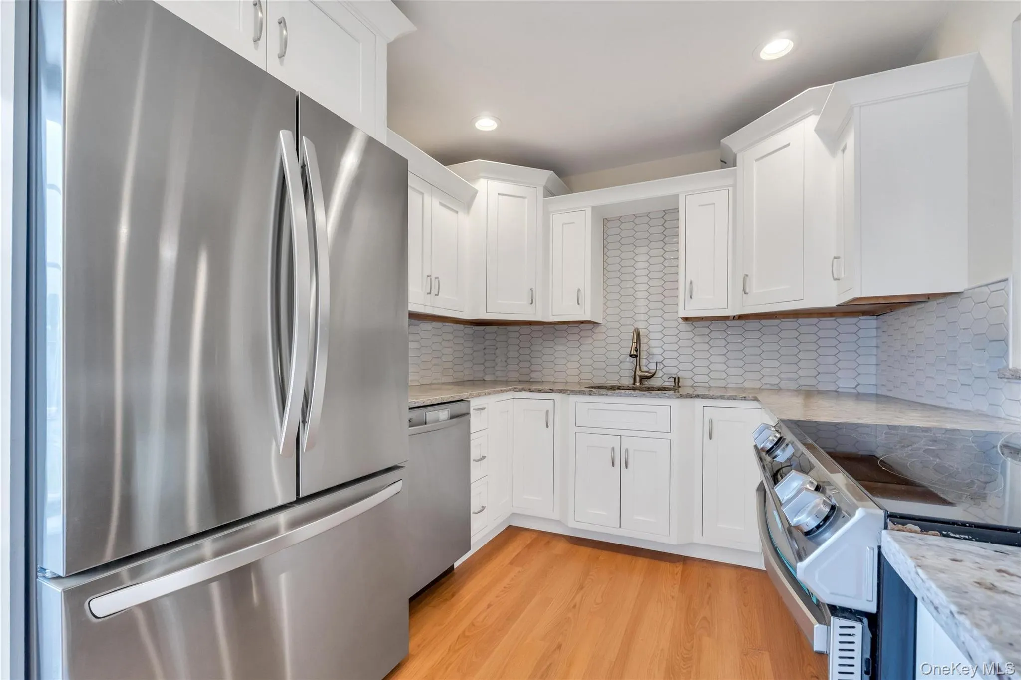 Modern kitchen featuring stainless steel appliances, white cabinetry, granite countertops, and hardwood flooring Modern kitchen featuring stainless steel appliances, white cabinetry, granite countertops, and hardwood flooring