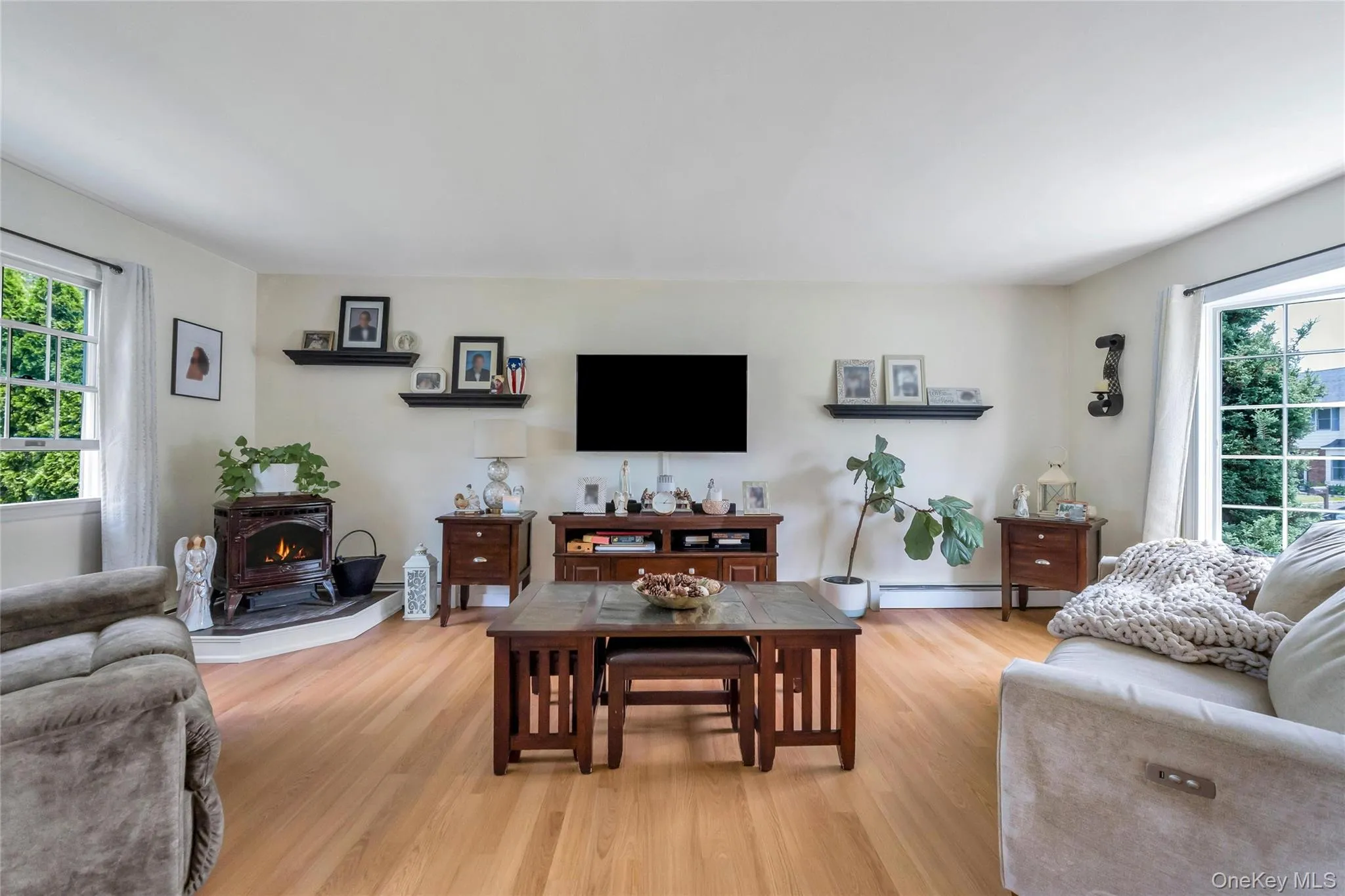 Spacious living area featuring light wood-finish flooring, a built-in pellet stove, and multiple large windows Spacious living area featuring light wood-finish flooring, a built-in pellet stove, and multiple large windows