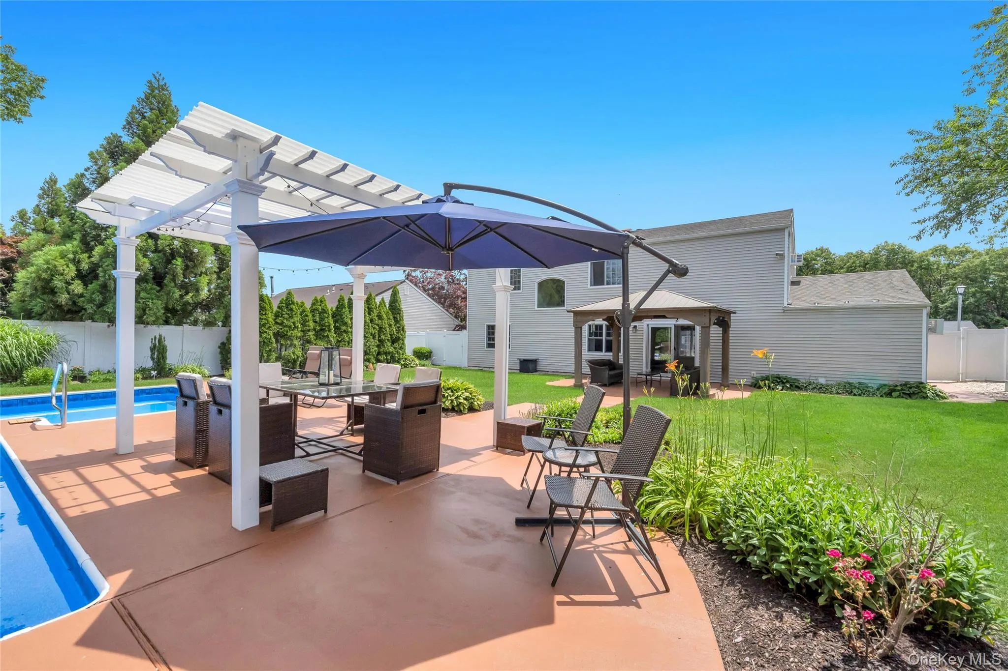 Expansive backyard featuring a large in-ground swimming pool, a spacious concrete patio, a white pergola structure, and a separate covered gazebo Expansive backyard featuring a large in-ground swimming pool, a spacious concrete patio, a white pergola structure, and a separate covered gazebo