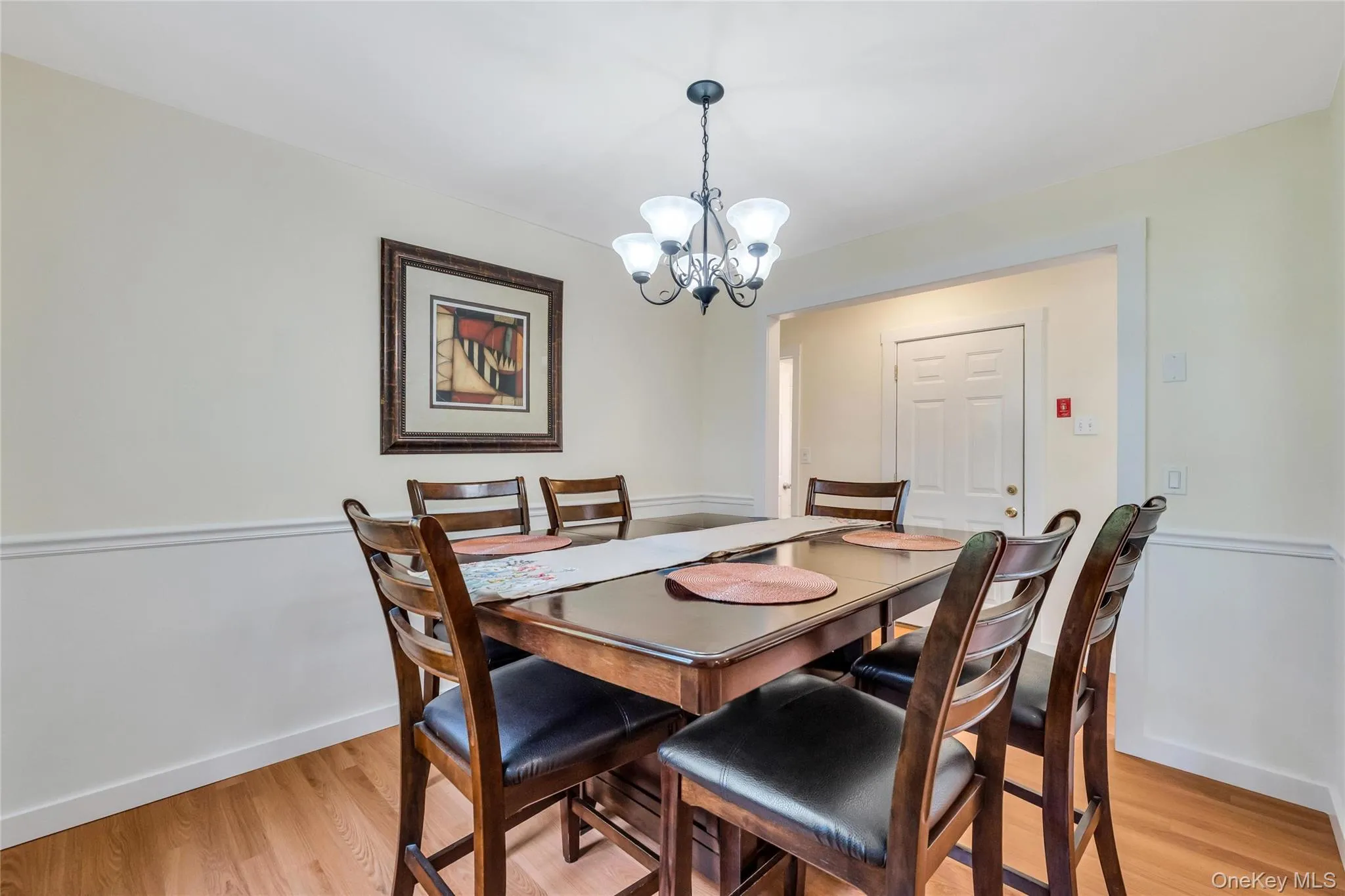Dining area featuring wood-finish flooring, wainscoting, and a multi-bulb chandelier Dining area featuring wood-finish flooring, wainscoting, and a multi-bulb chandelier