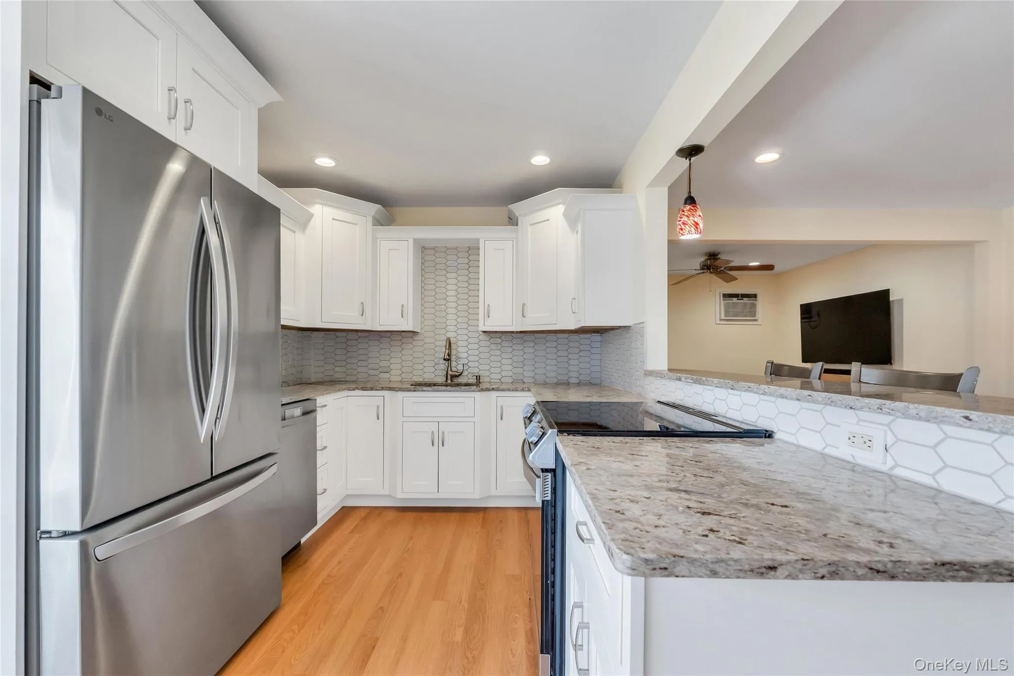 Modern kitchen featuring white cabinetry, stainless steel appliances, wood-finish flooring, granite countertops, and a subway tile backsplash Modern kitchen featuring white cabinetry, stainless steel appliances, wood-finish flooring, granite countertops, and a subway tile backsplash