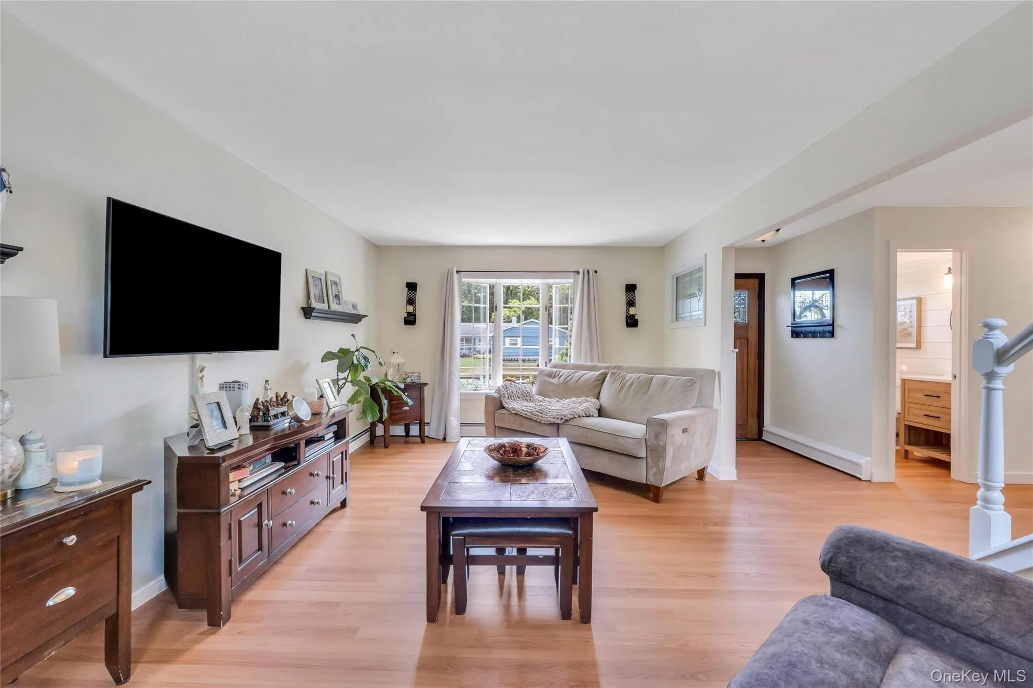 Open-concept living area featuring light wood-finish flooring, a neutral color palette, and a sliding glass door providing natural light Open-concept living area featuring light wood-finish flooring, a neutral color palette, and a sliding glass door providing natural light