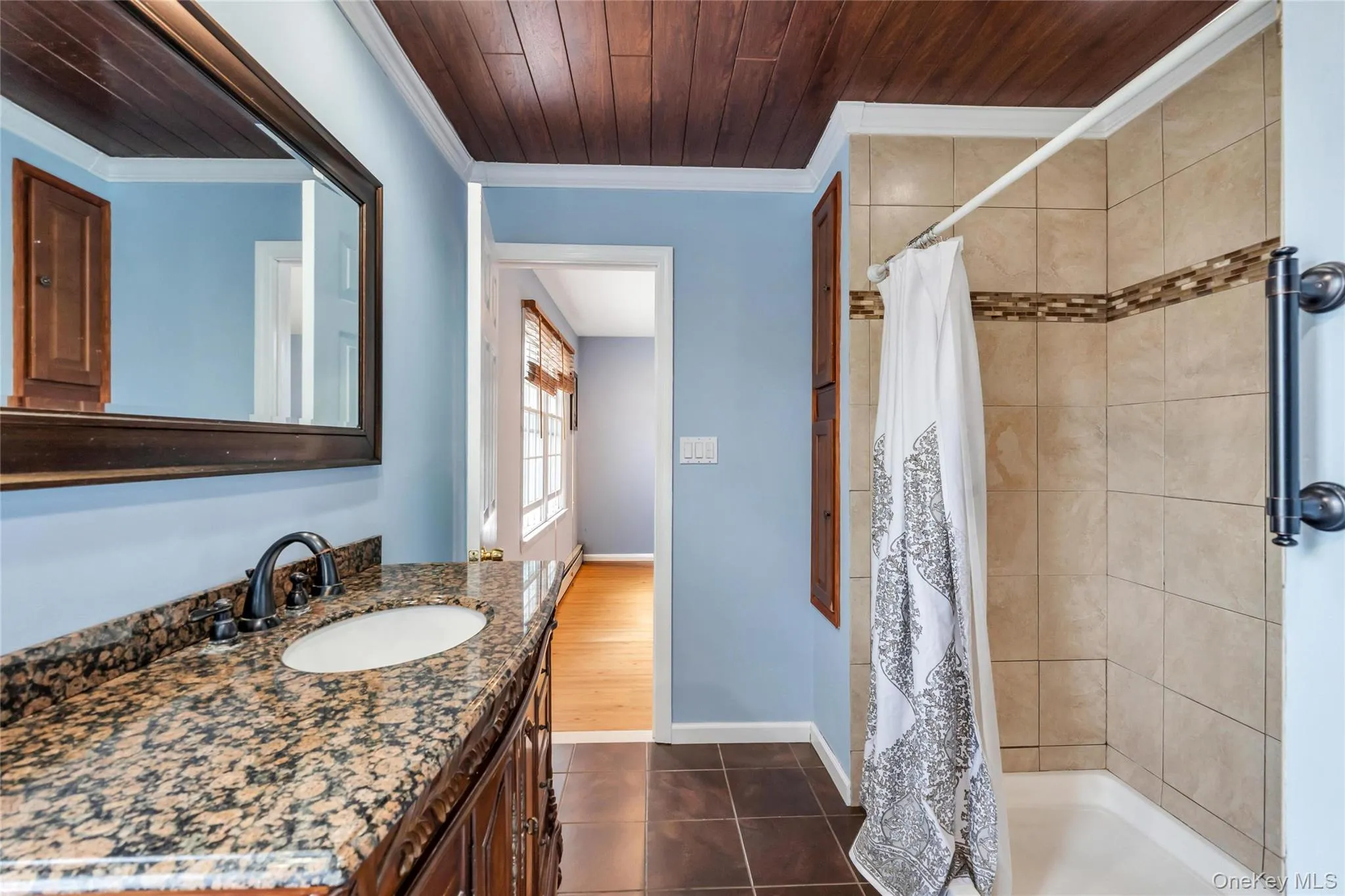 Bathroom featuring a dark wood plank ceiling, light blue walls, and brown floor tiling Bathroom featuring a dark wood plank ceiling, light blue walls, and brown floor tiling